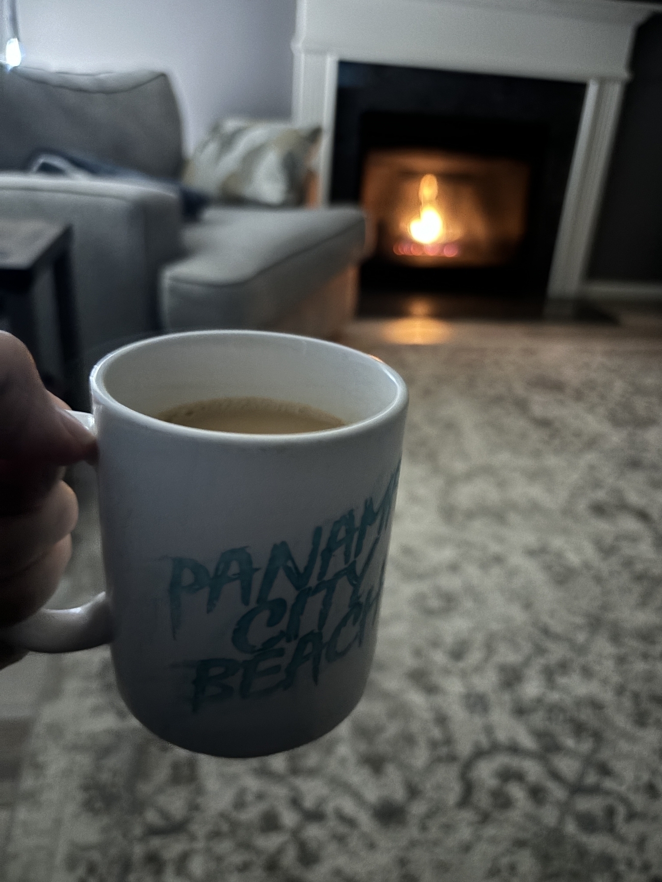 A white mug that reads, “Panama city beach” in a cozy living room in front of a fire