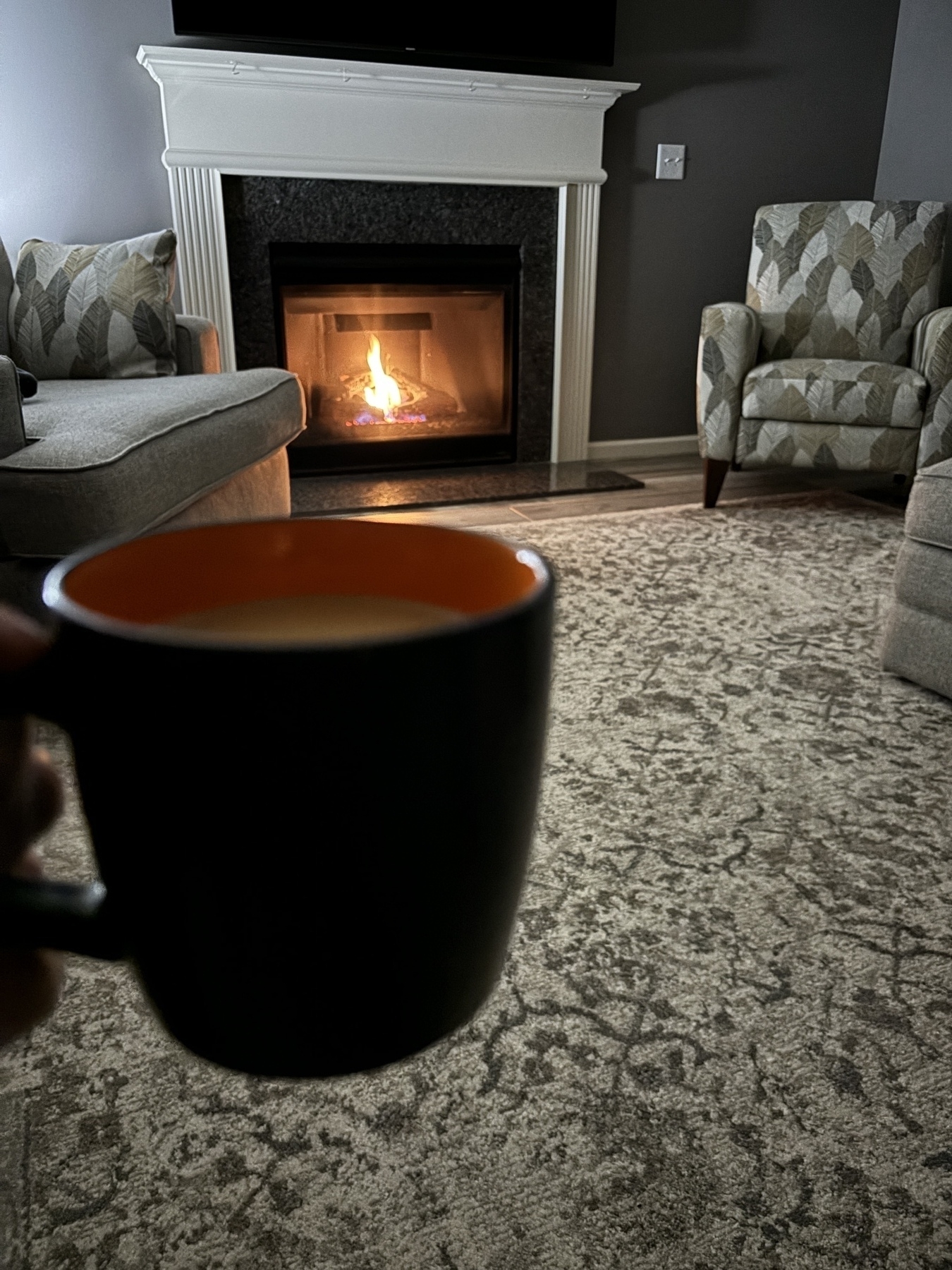 A black and orange coffee mug in front of an inviting fire. 