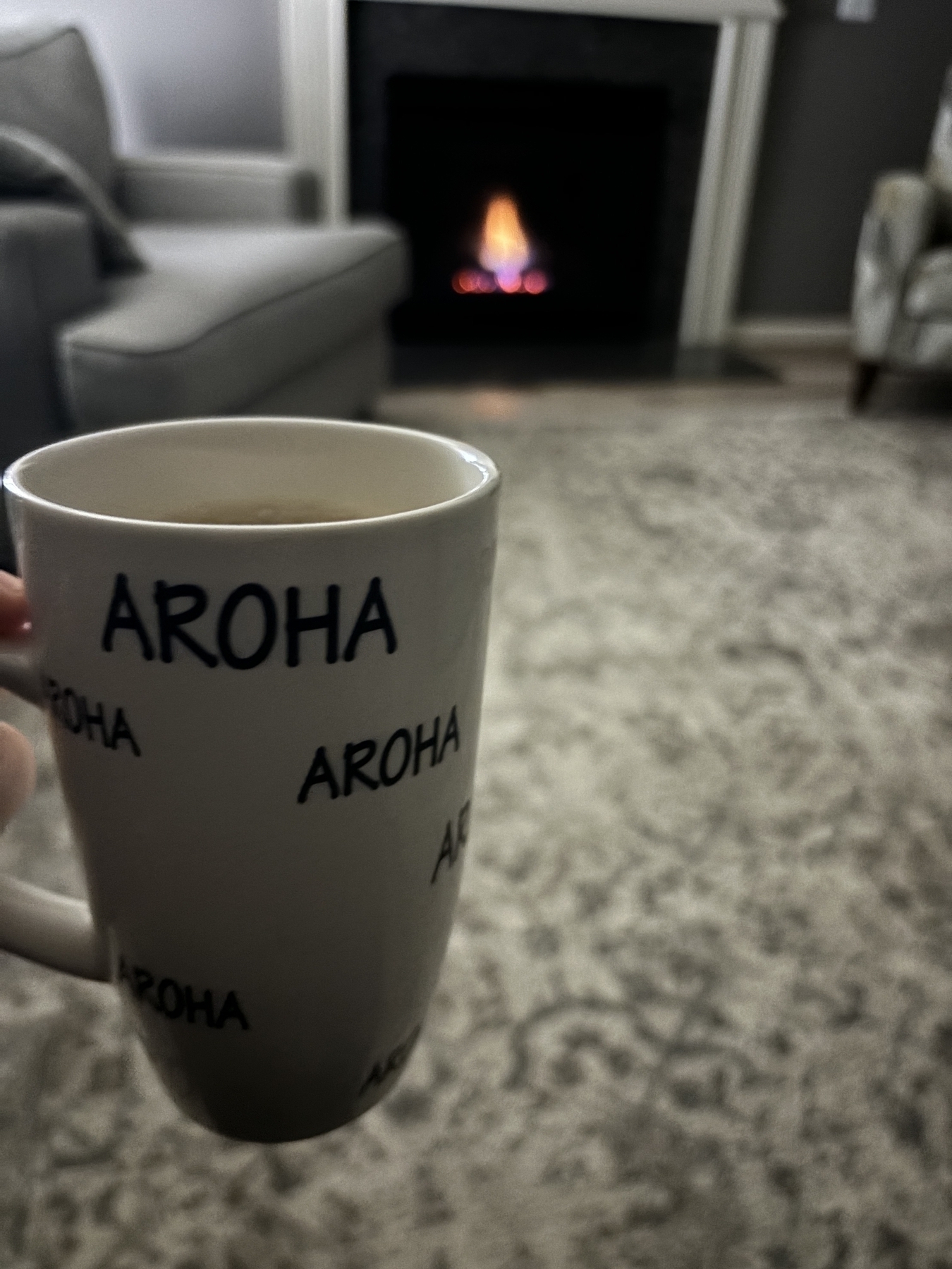 A coffee mug that says, “Aroha” which is “love” in Māori in front of a welcoming fire. 
