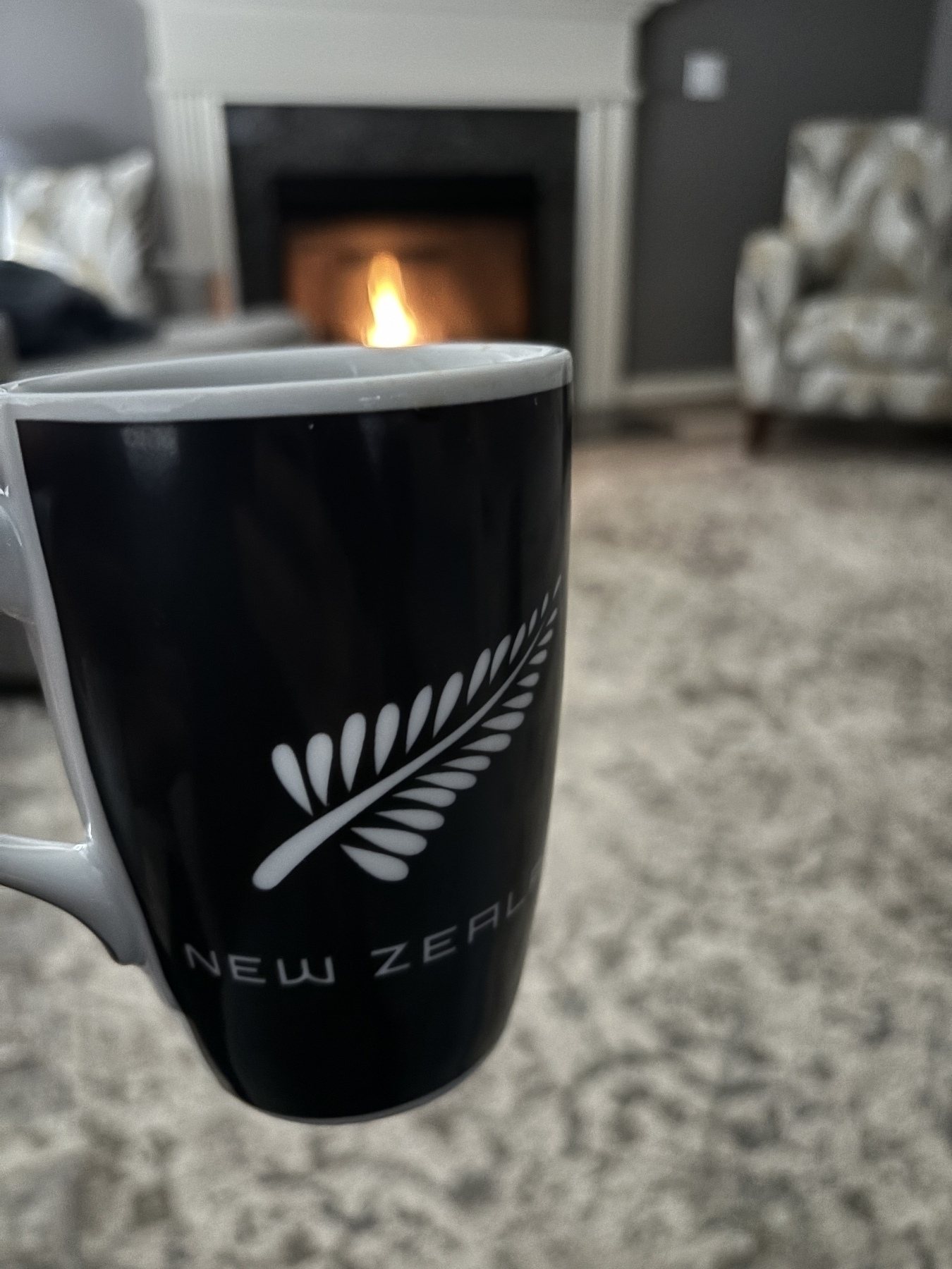 A New Zealand All Blacks coffee mug in front of a fire 