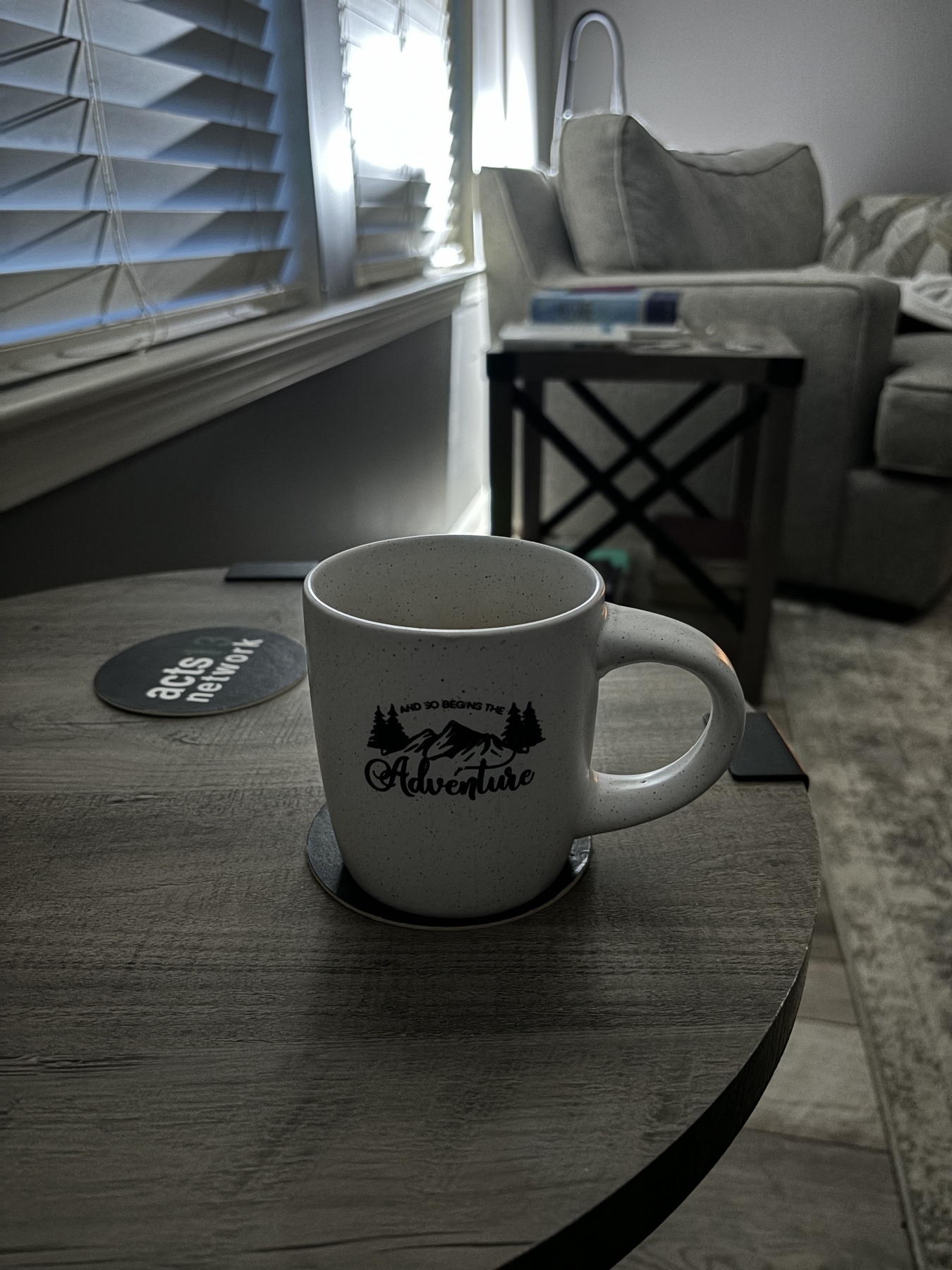 A coffee mug on side table. The coffee mug reads, “let the adventure begin.”