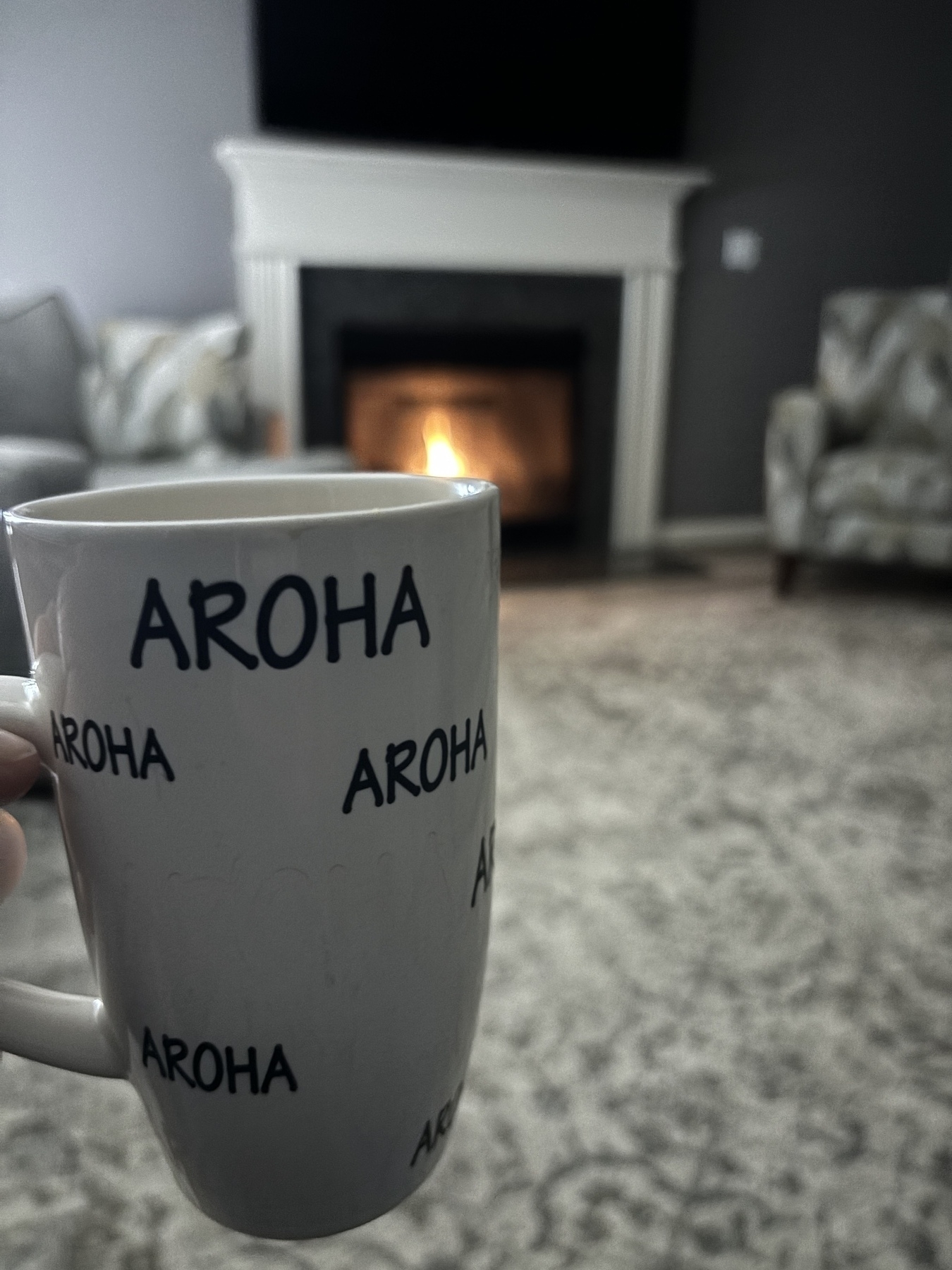 A coffee mug with the Māori word, “Aroha” on it in front of a welcoming fire 