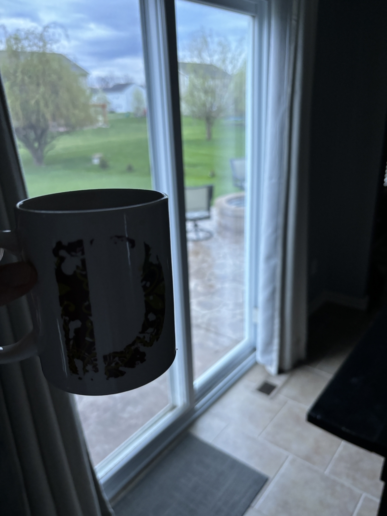 A coffee mug in front of a door wall overlooking a backyard 