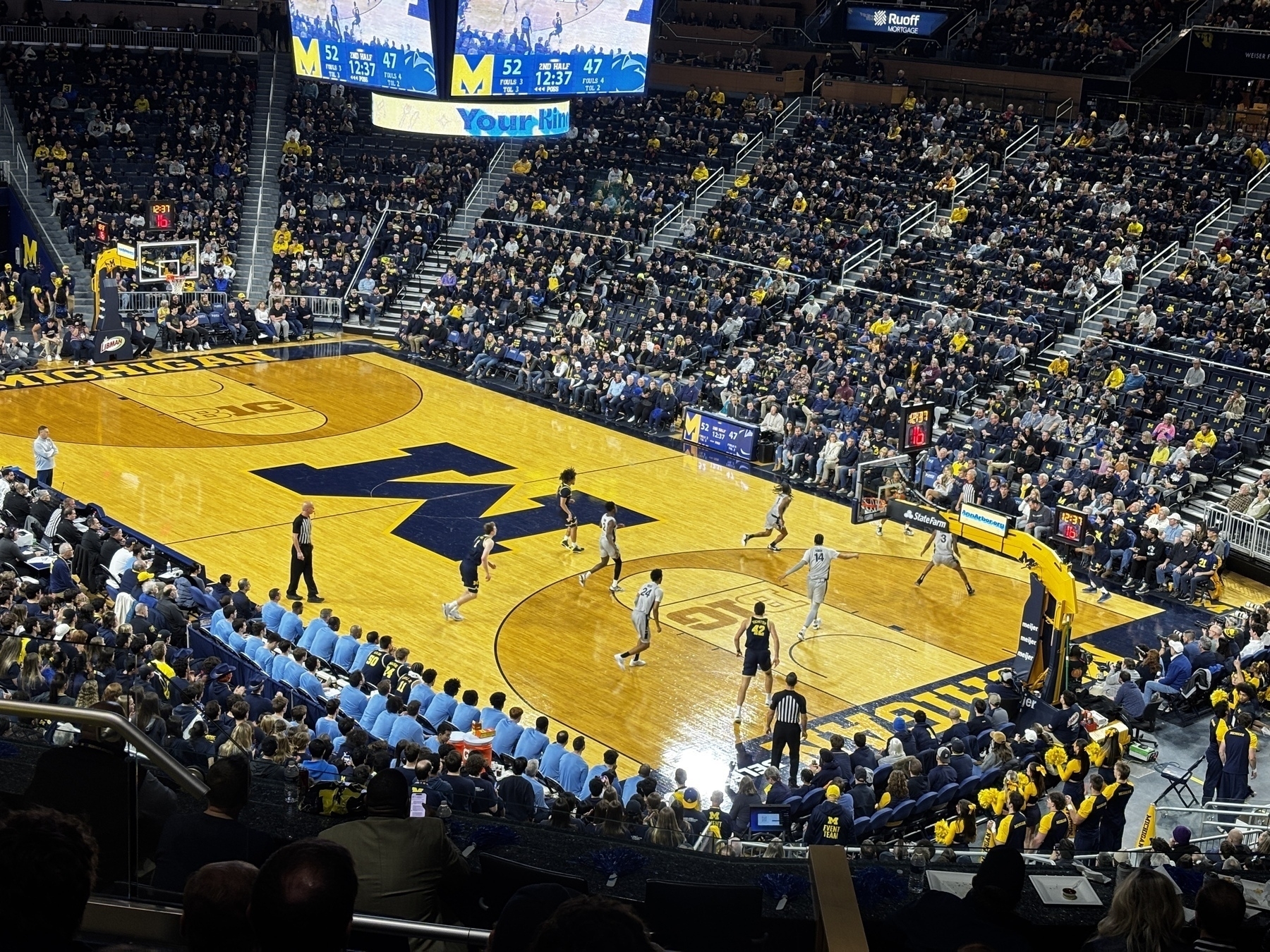 A basketball game is taking place in an arena with players in action and spectators watching.