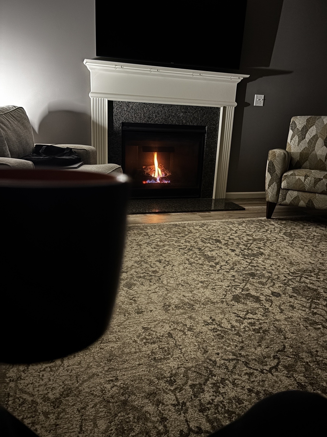 A coffee mug being held in a comfy living room with a cozy fire. 