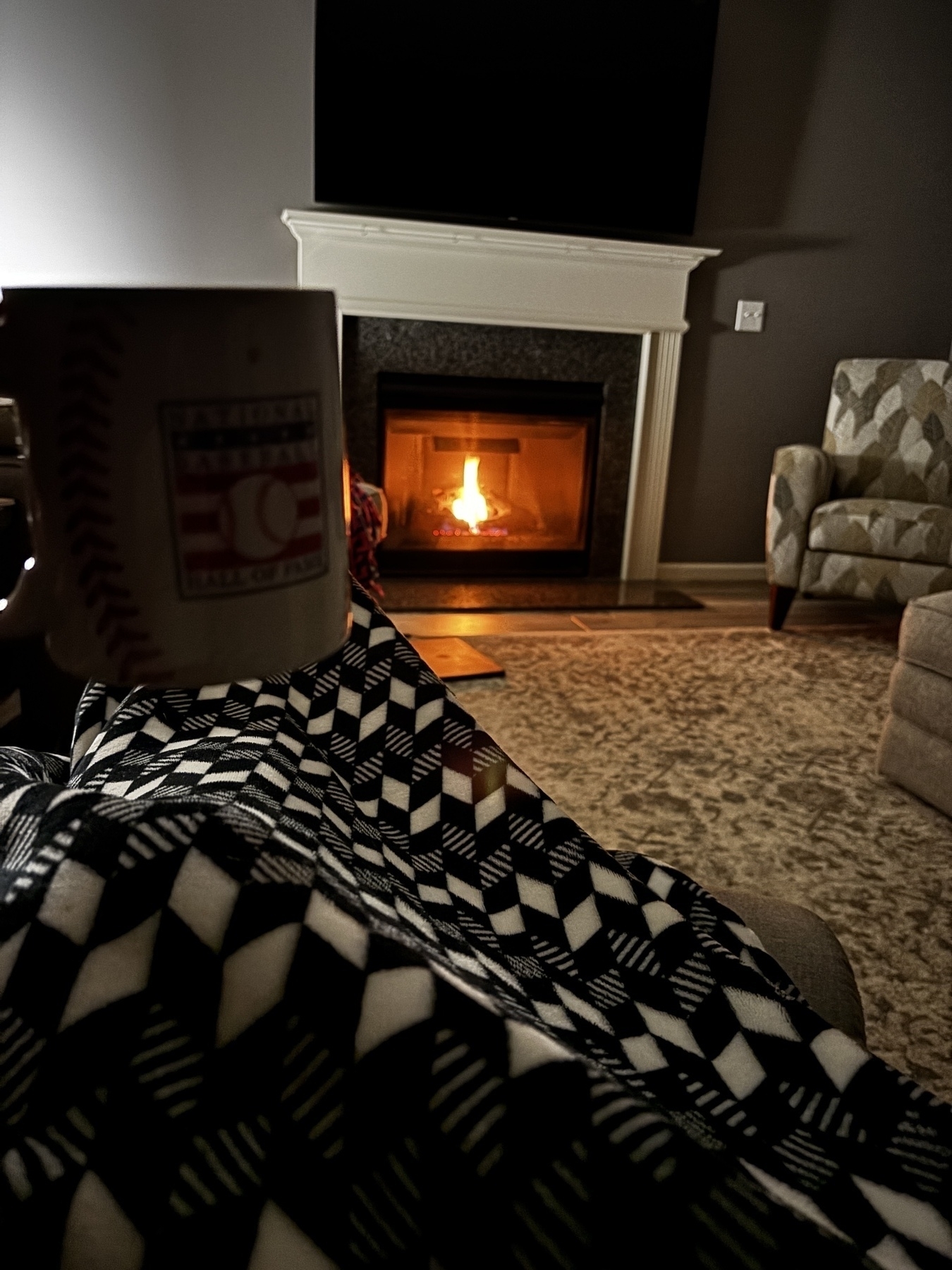 Cozy scene with a warm fireplace, a person relaxing under a blanket, and holding a mug.