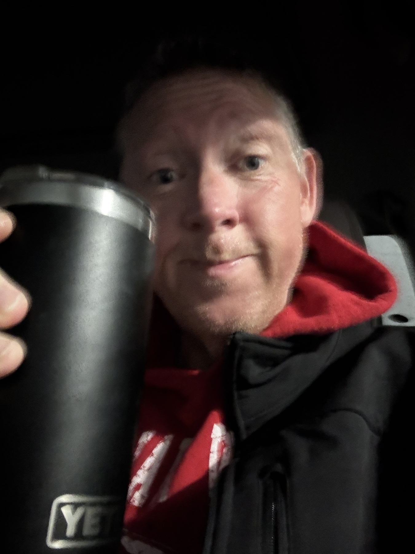 A person is holding a black YETI tumbler and wearing a red hoodie and a jacket.