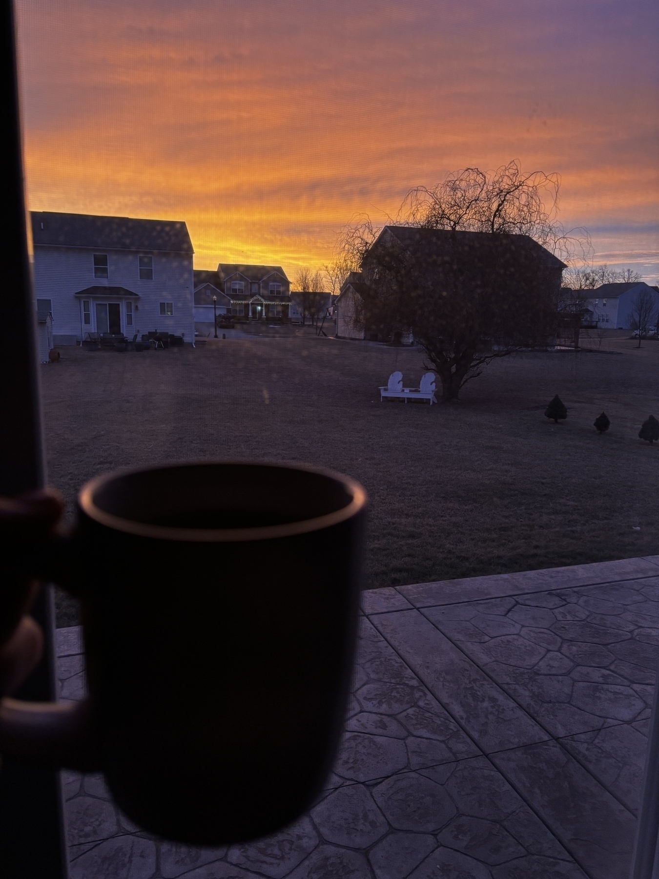 A coffee mug being held  with a sunrise that defies imagination in its beauty of oranges, pinks and purples in the background. 