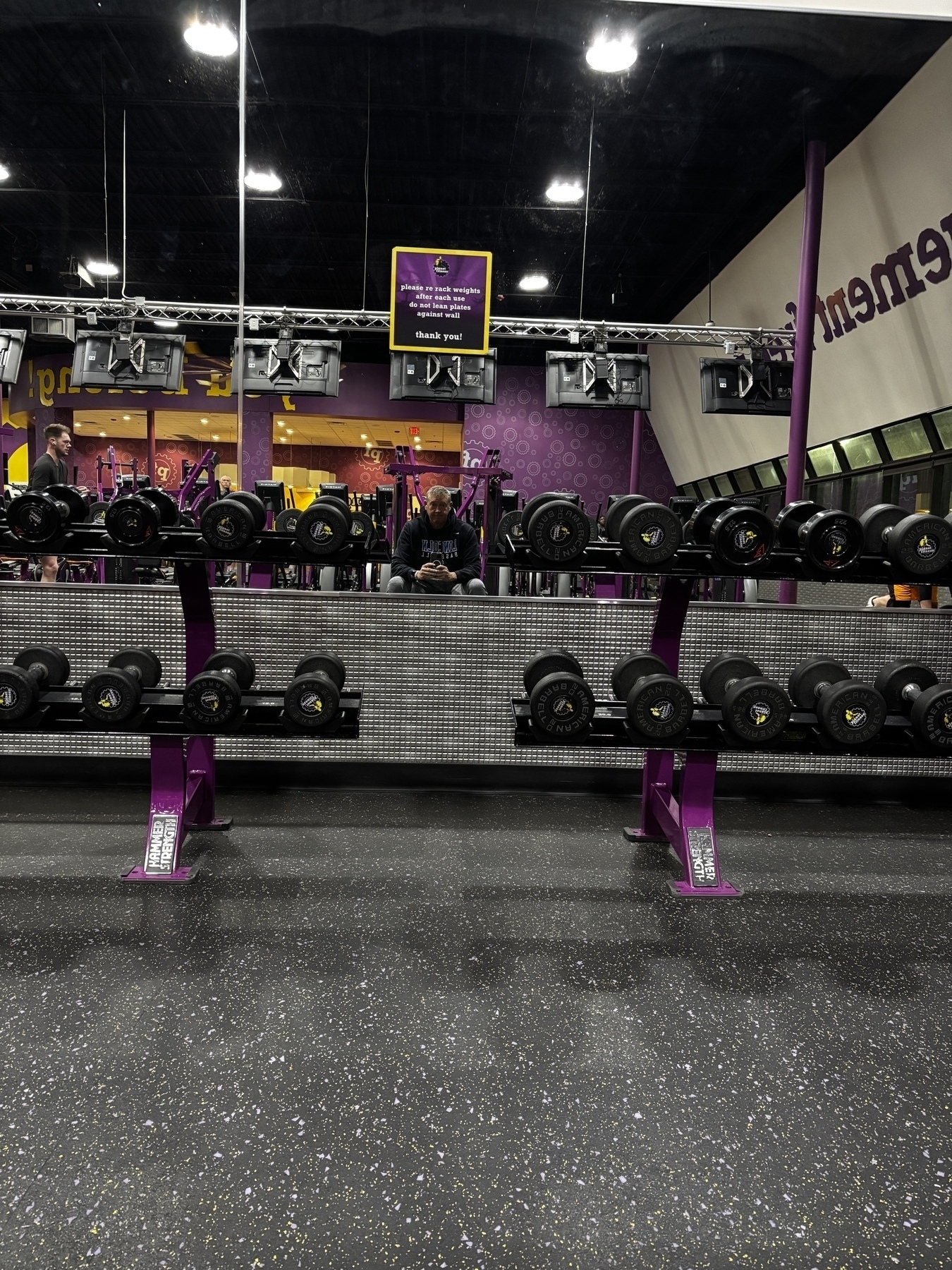 A gym setup featuring a wide range of dumbbells neatly organized in front of a large mirror.