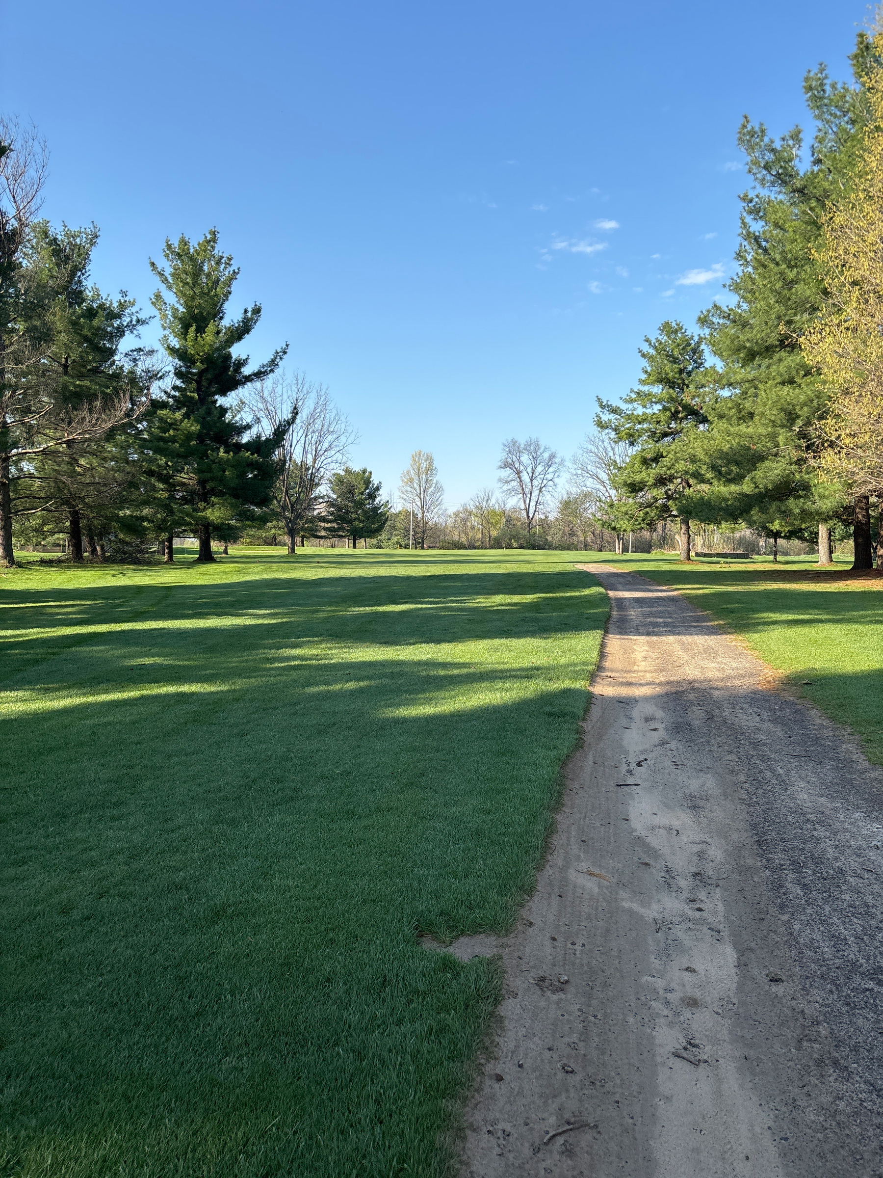 A dirt path runs through a green park lined with trees under a clear blue sky at PineView Golf course