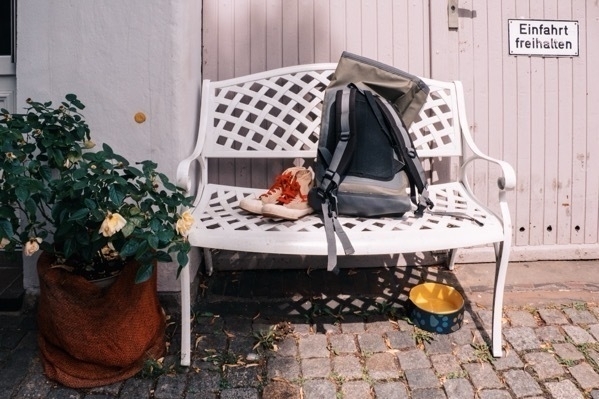 Eine Bank, im Bremer Schnoorviertel, vor einer Garage. Auf der Bank stehen Schuhe und ein Rucksack. Darunter ein Wassernapf.