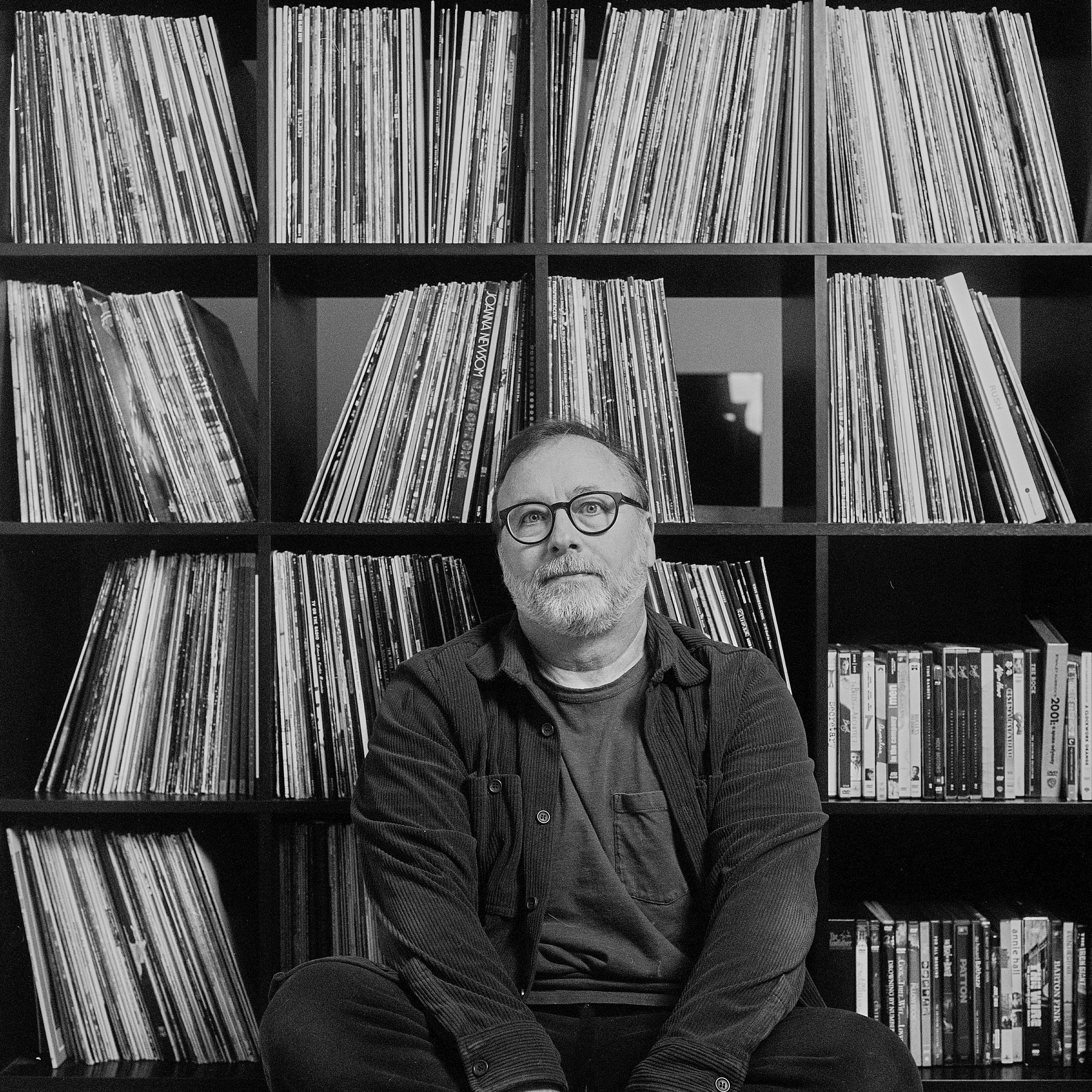 Black and white film self-portrait sitting in front of the record shelves