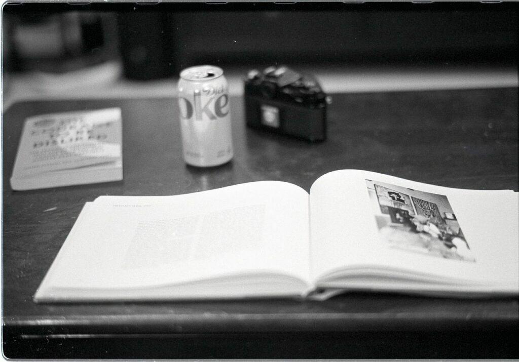 Out of focus, dusty black and white photo of book, camera, pop can, etc on my coffee table.