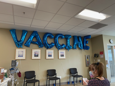 The waiting room at Kaiser - time to get the first shot! On the wall, spelled out in mylar balloons, the word VACCINE.