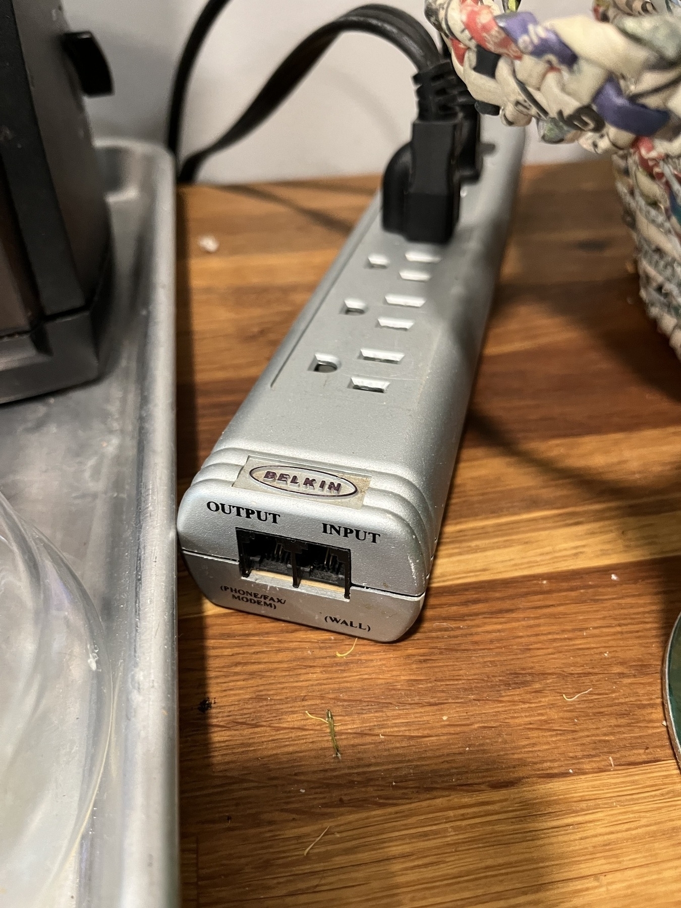 A grey Belkin-branded power strip with two slots for phone cables. One labeled Output (Phone/Fax/Modem) and one labeled Input (Wall).