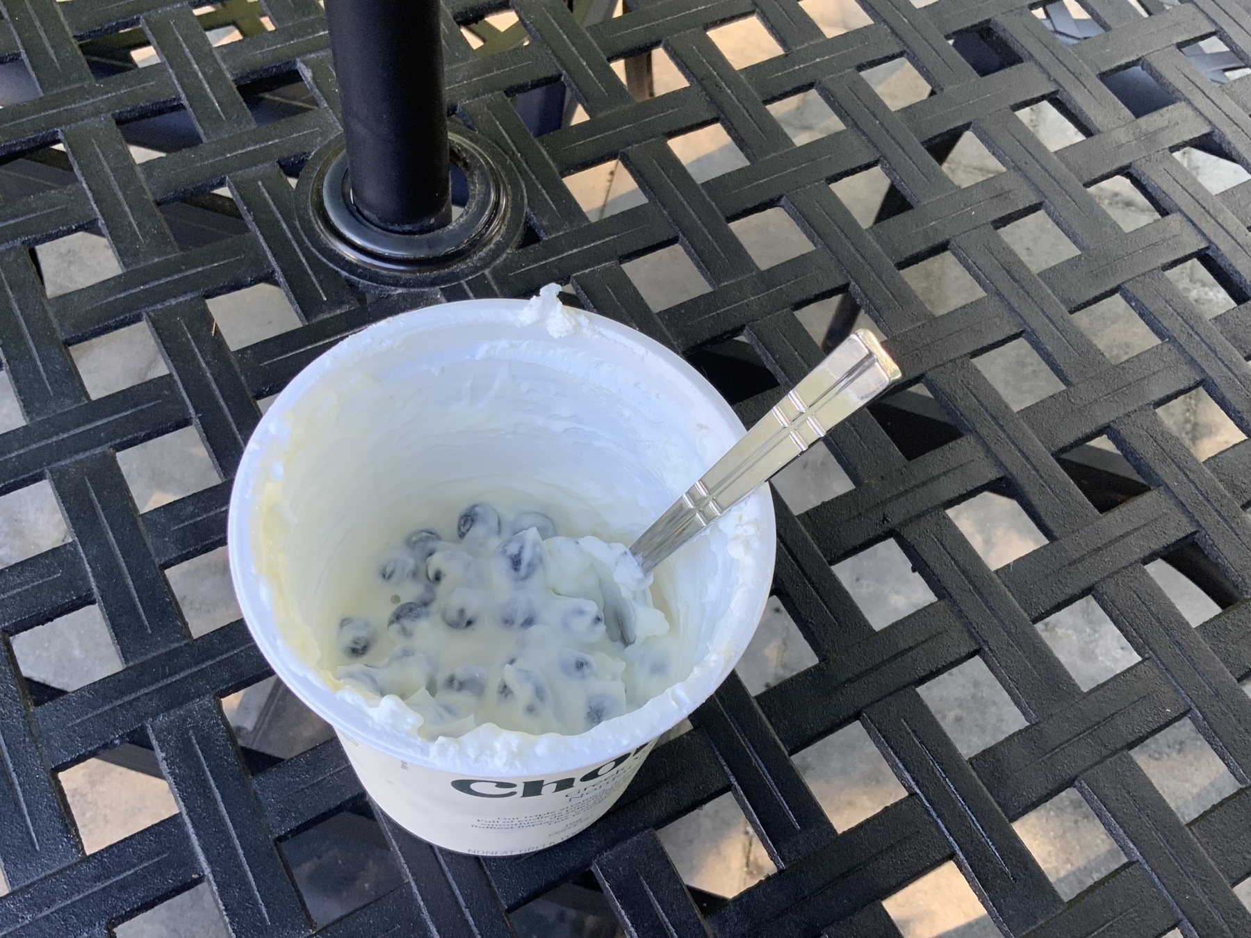 A tub of Chobani Nonfat Plain Greek Yogurt with a spoon sticking out of it. Within the yogurt are a large amount of blueberries.