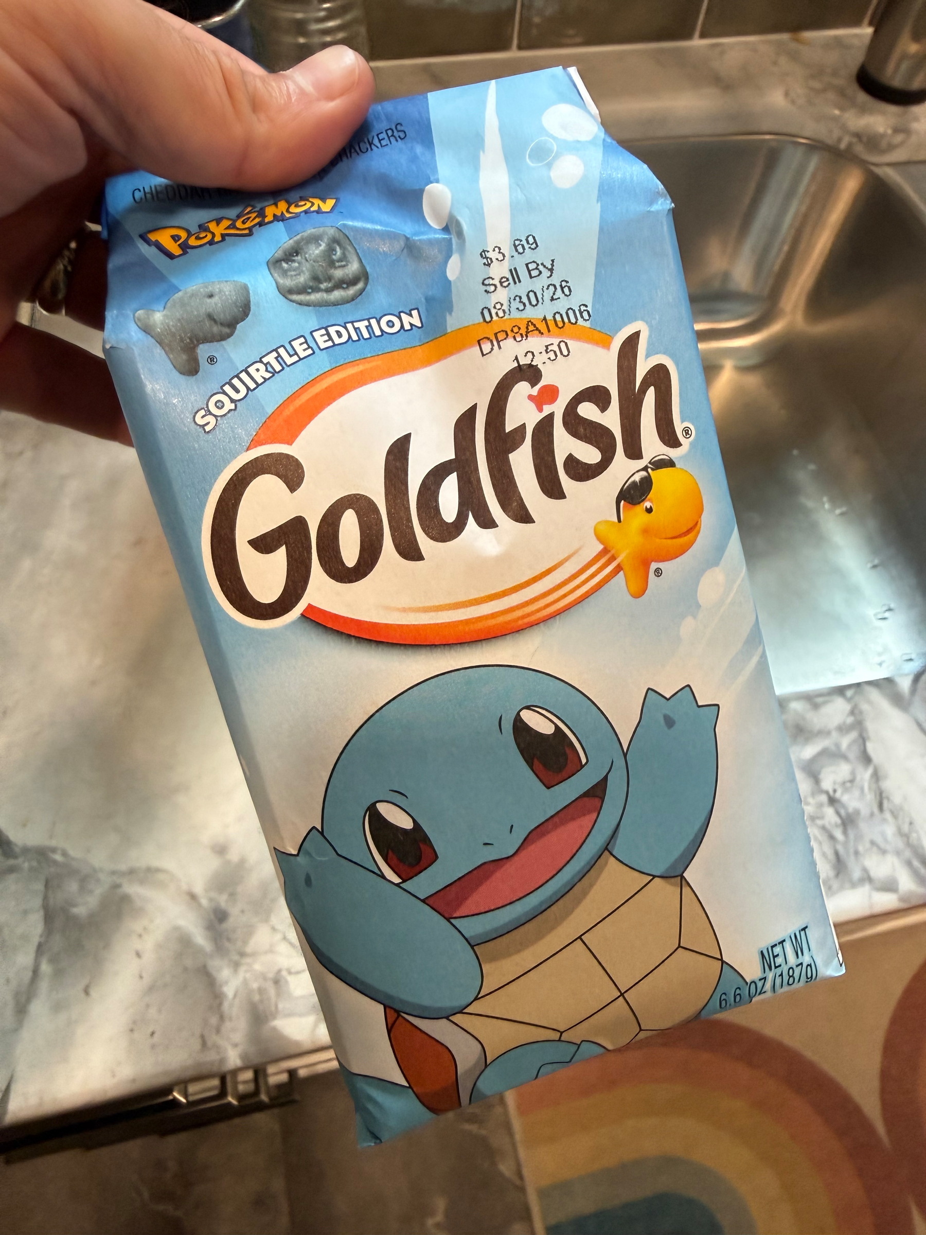 A hand is holding a blue package of Pokémon Squirtle Edition Goldfish crackers above a kitchen sink.