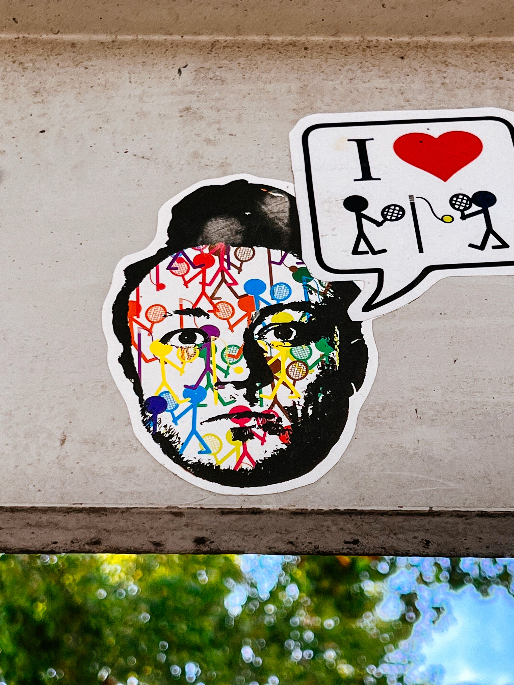 Sticker of what looks like the face of Conan O’Brien, with rainbow colored tennis playing stick figures all over his face.