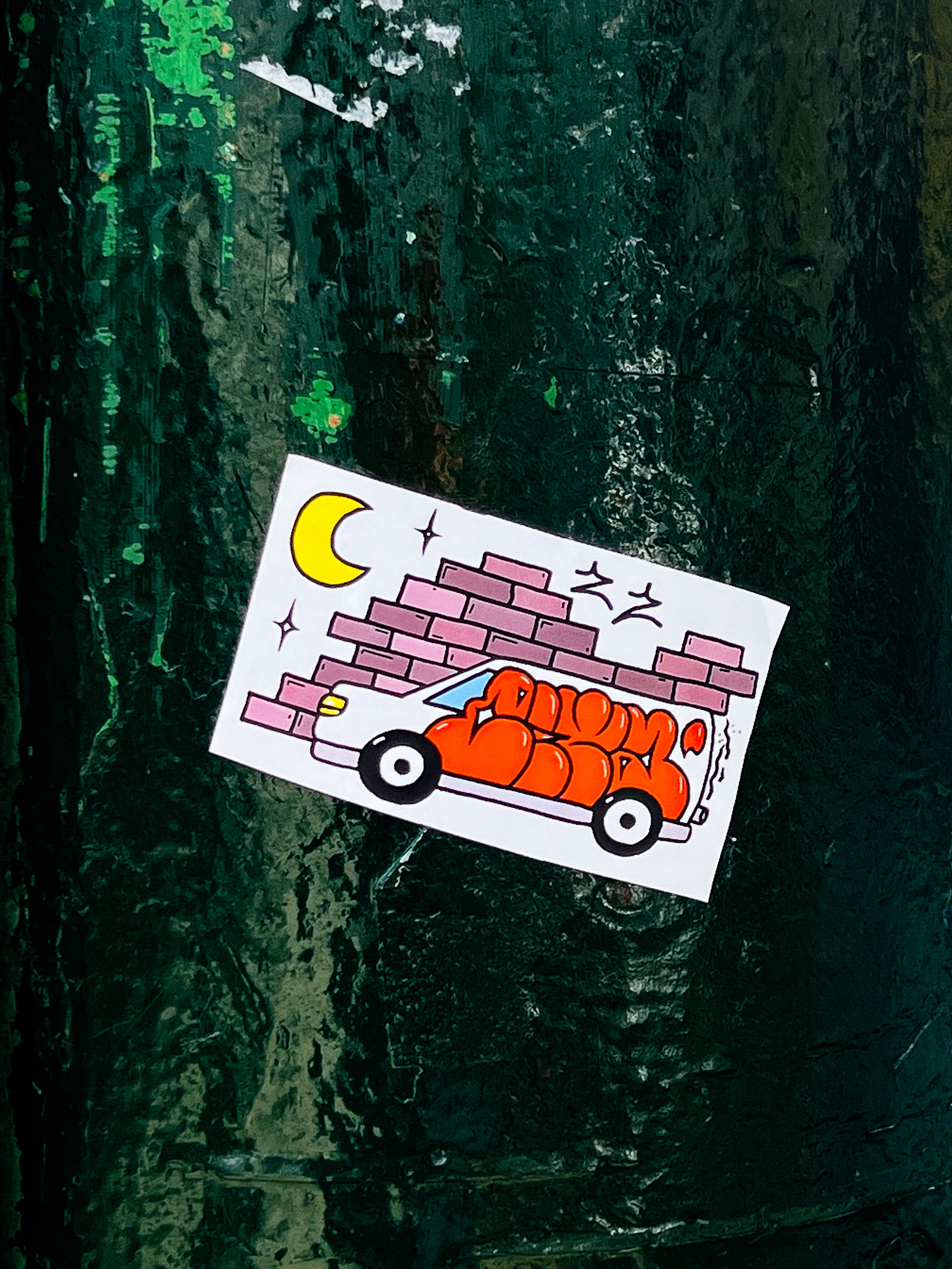 Sticker with a crude drawing of a van with graffiti, in front of a brick wall, and a moon. 