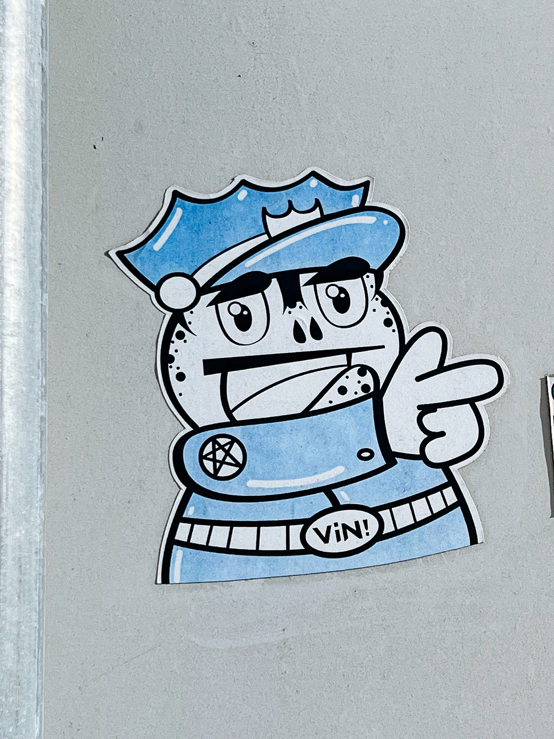 Sticker of a cartoon frog dressed as a policeman, using his hand as a gun. 