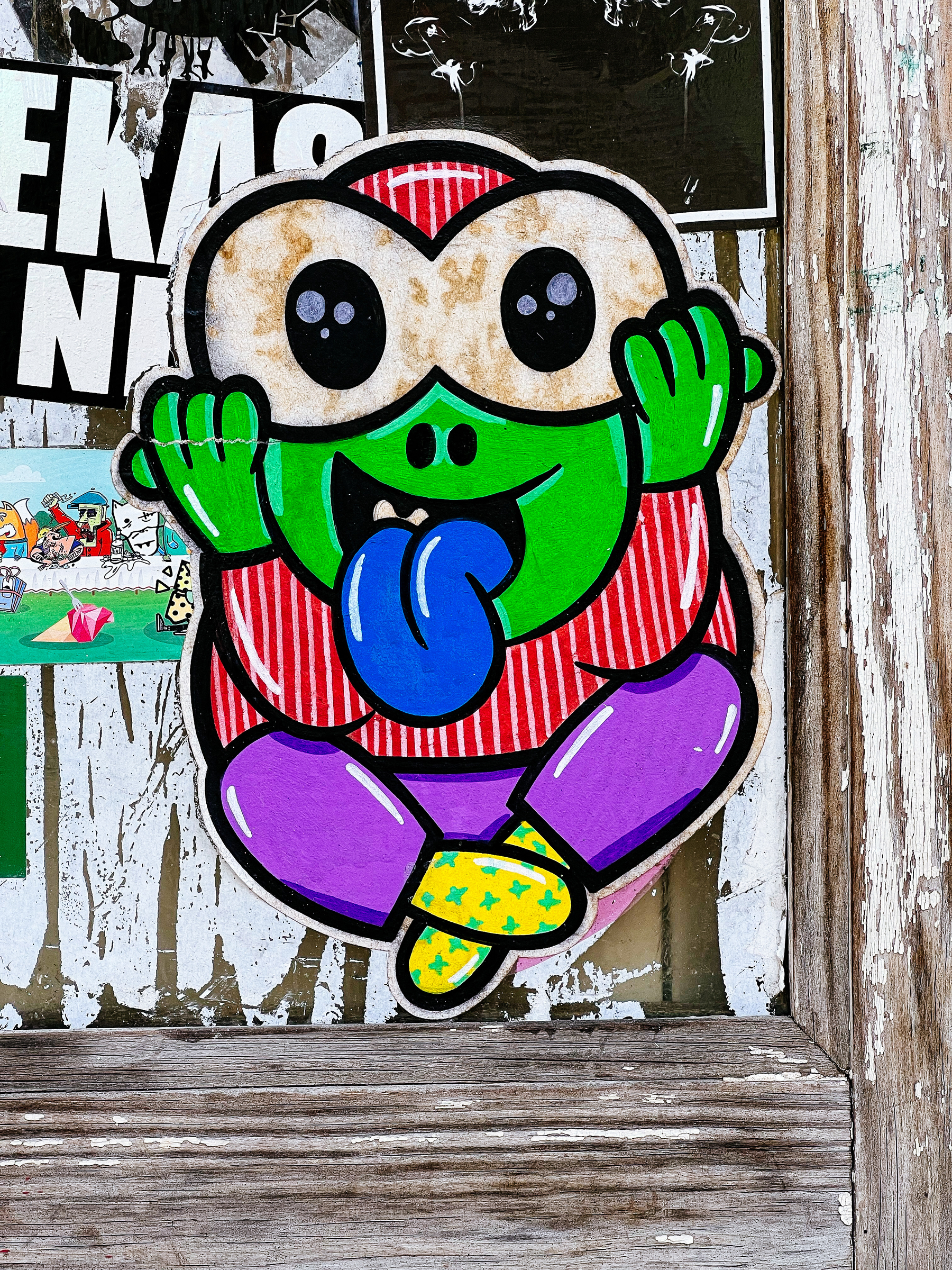 Sticker of a crazy looking cartoon frog, sticking his blue tongue out at us. 
