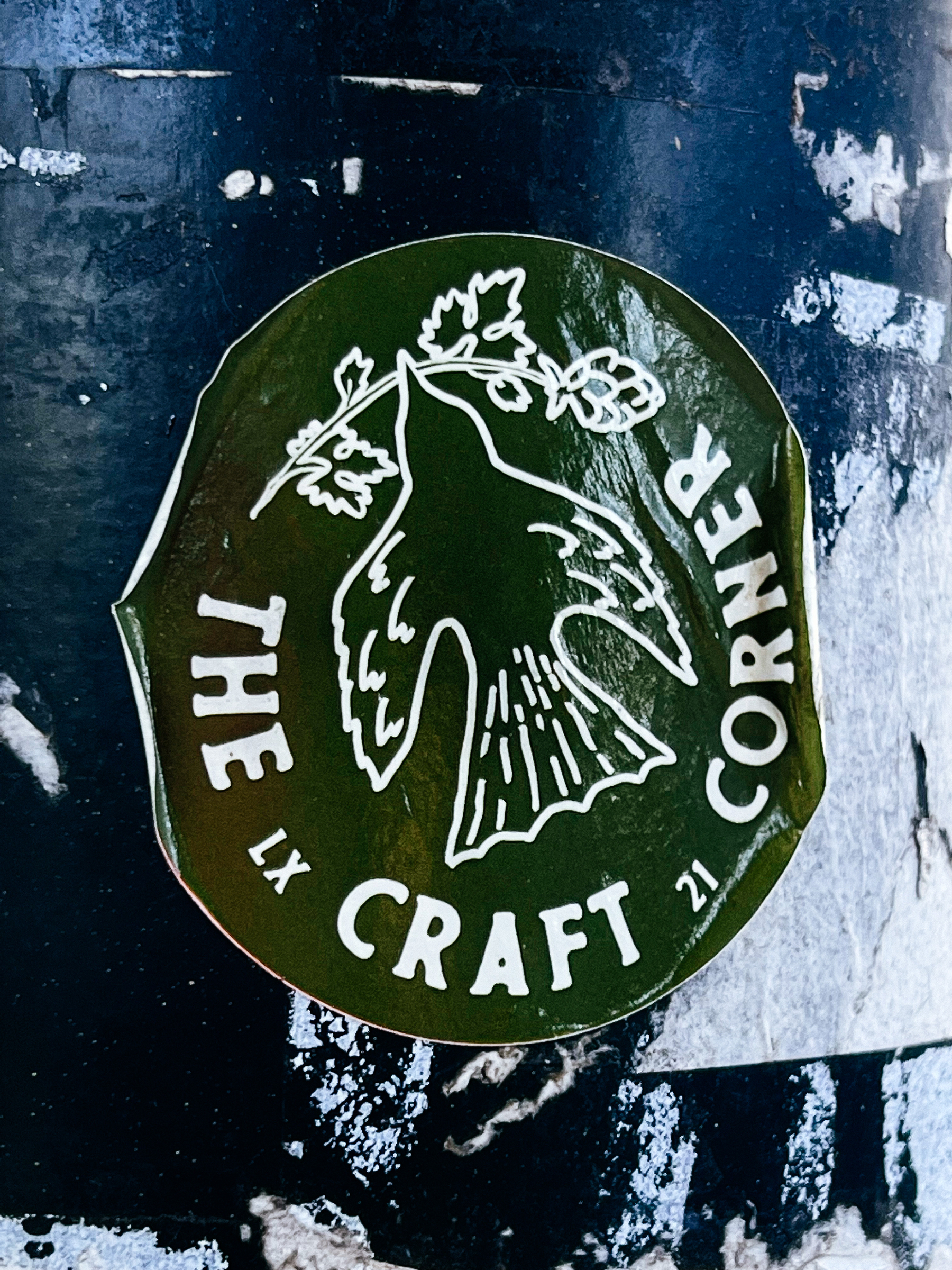 Sticker of a bird flying with a branch on the beak, and the words “The Craft Corner”.