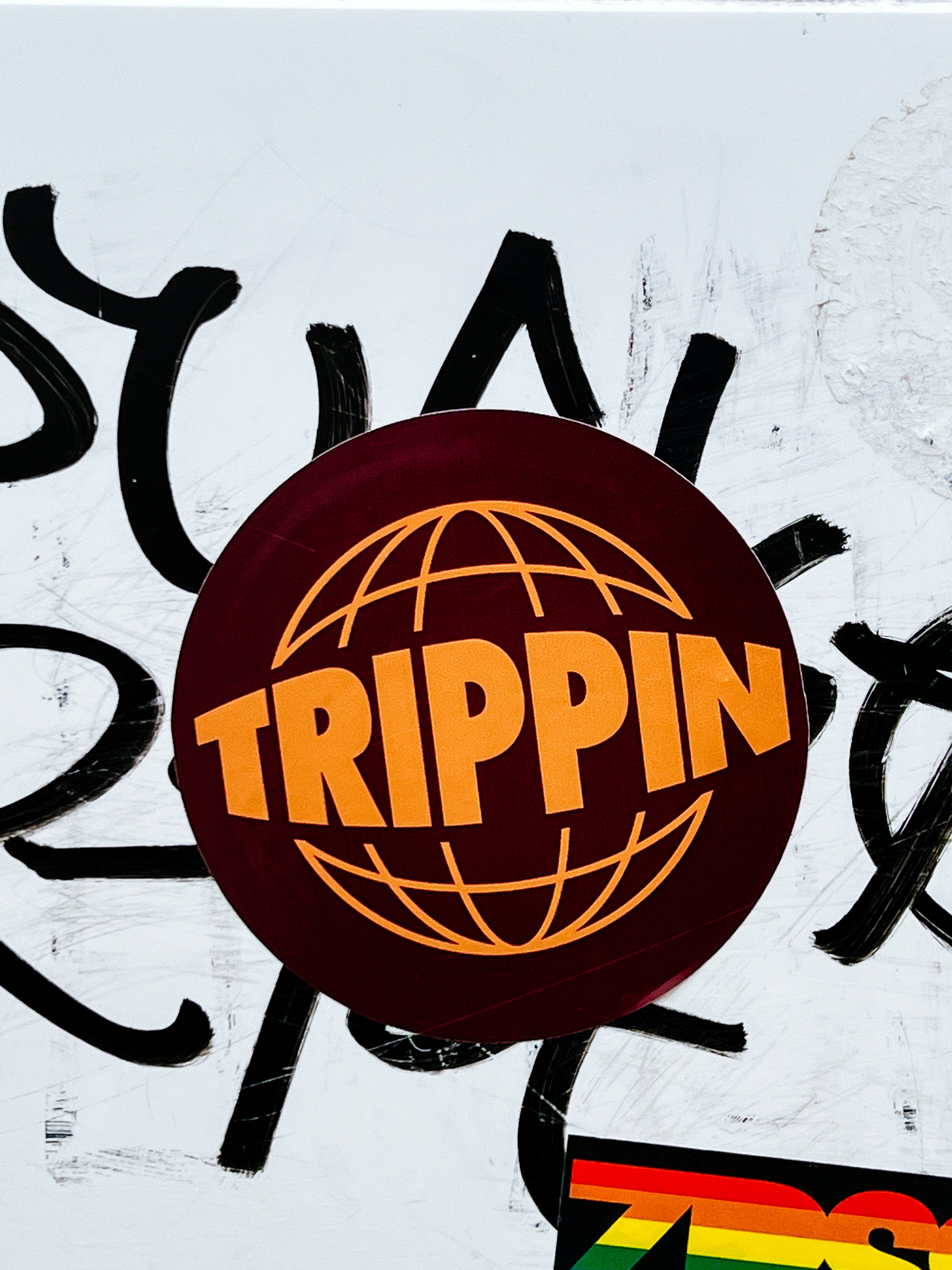 Sticker with the drawing of a globe, and the word “Trippin” written over it. 