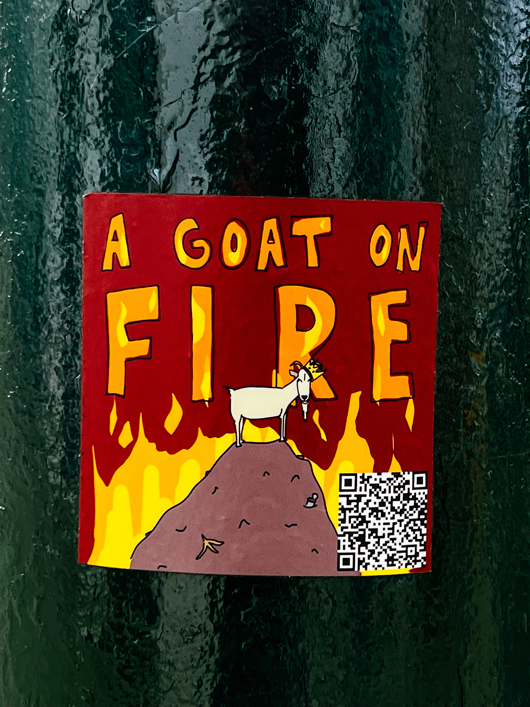 Sticker with the words “A Goat on Fire”, and the drawing of a goat standing on top of a burning pile of trash. 