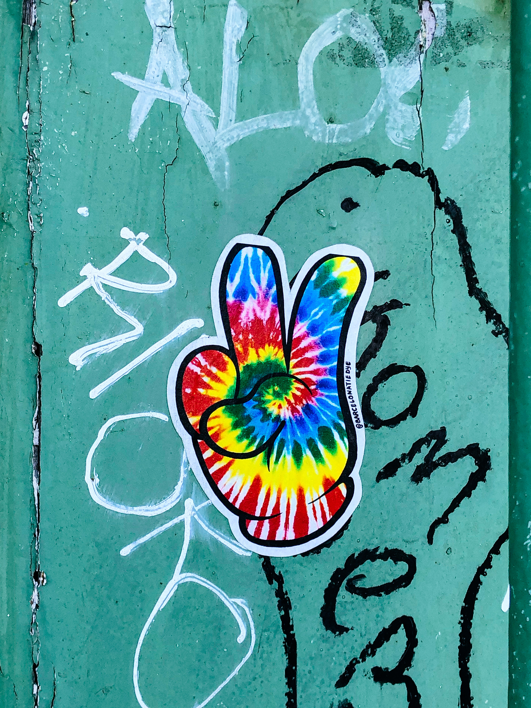 Sticker of a tie-dye cartoon hand doing the V sign. 