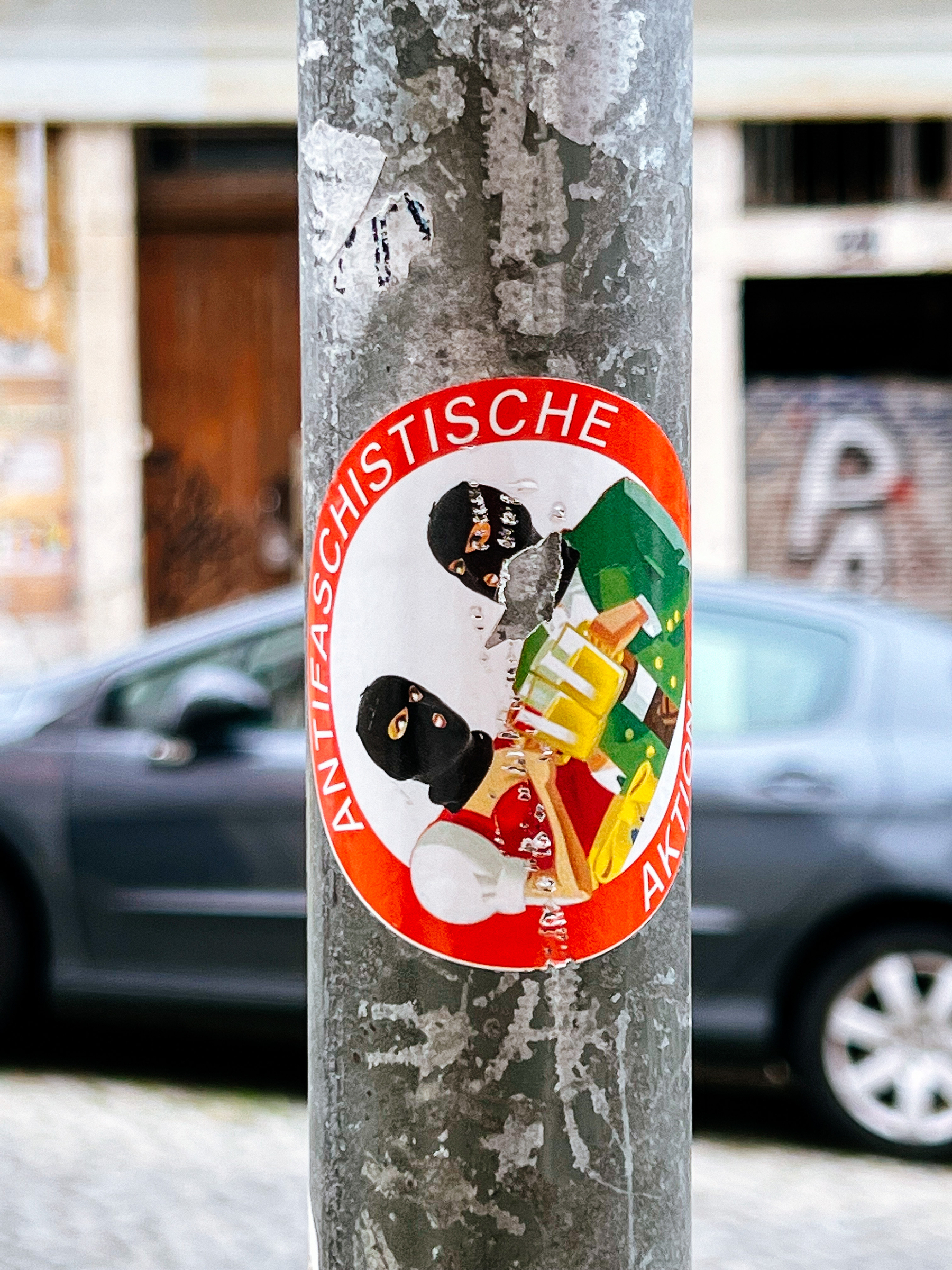 A sticker where a man and a woman toast with beer, both wearing balaclava masks. The word “Antifaschistische” is showing on the edge of the sticker.