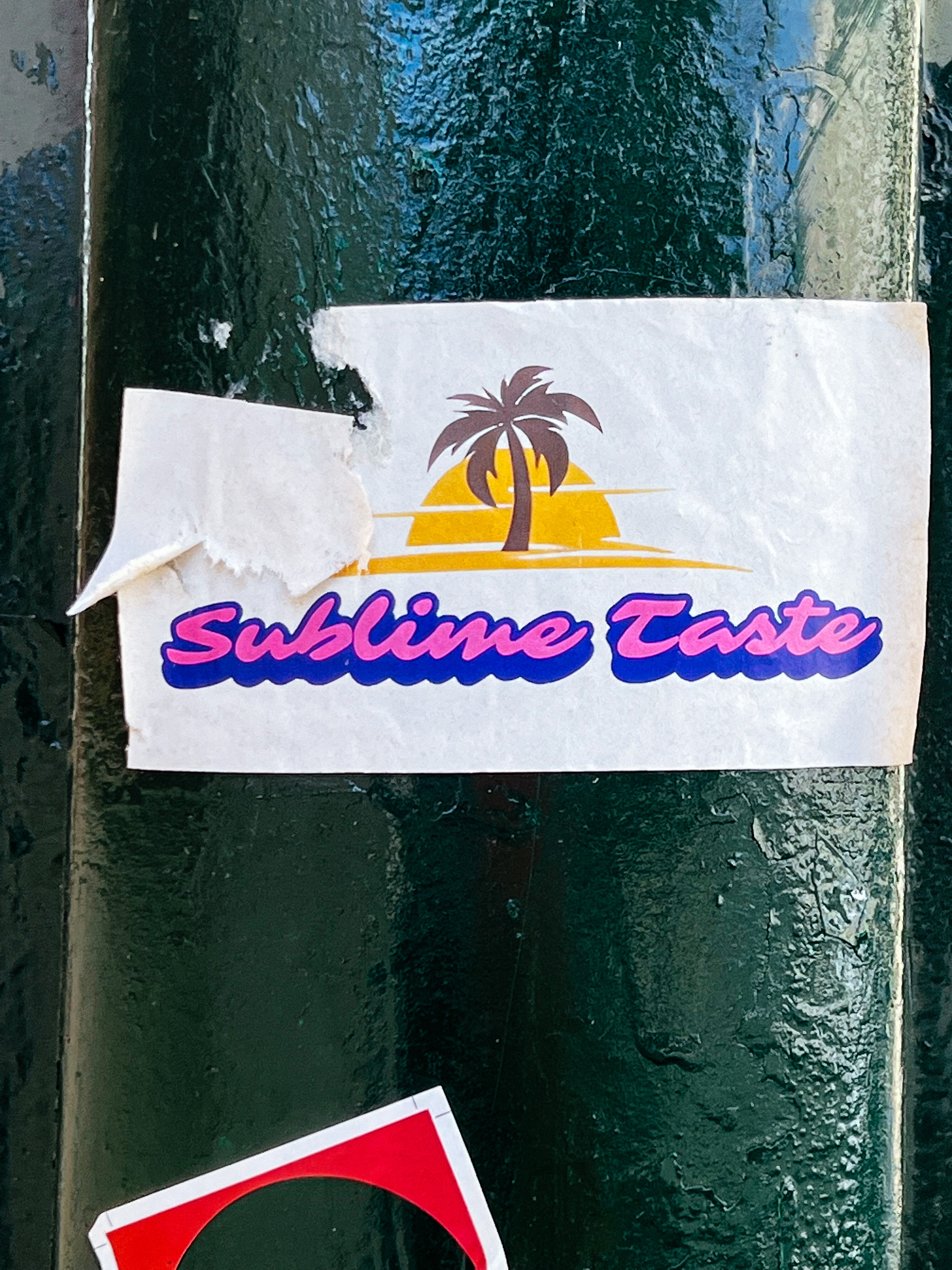 Sticker of a palm tree in front of a sunset, with the words “Sublime Taste” written under it. 