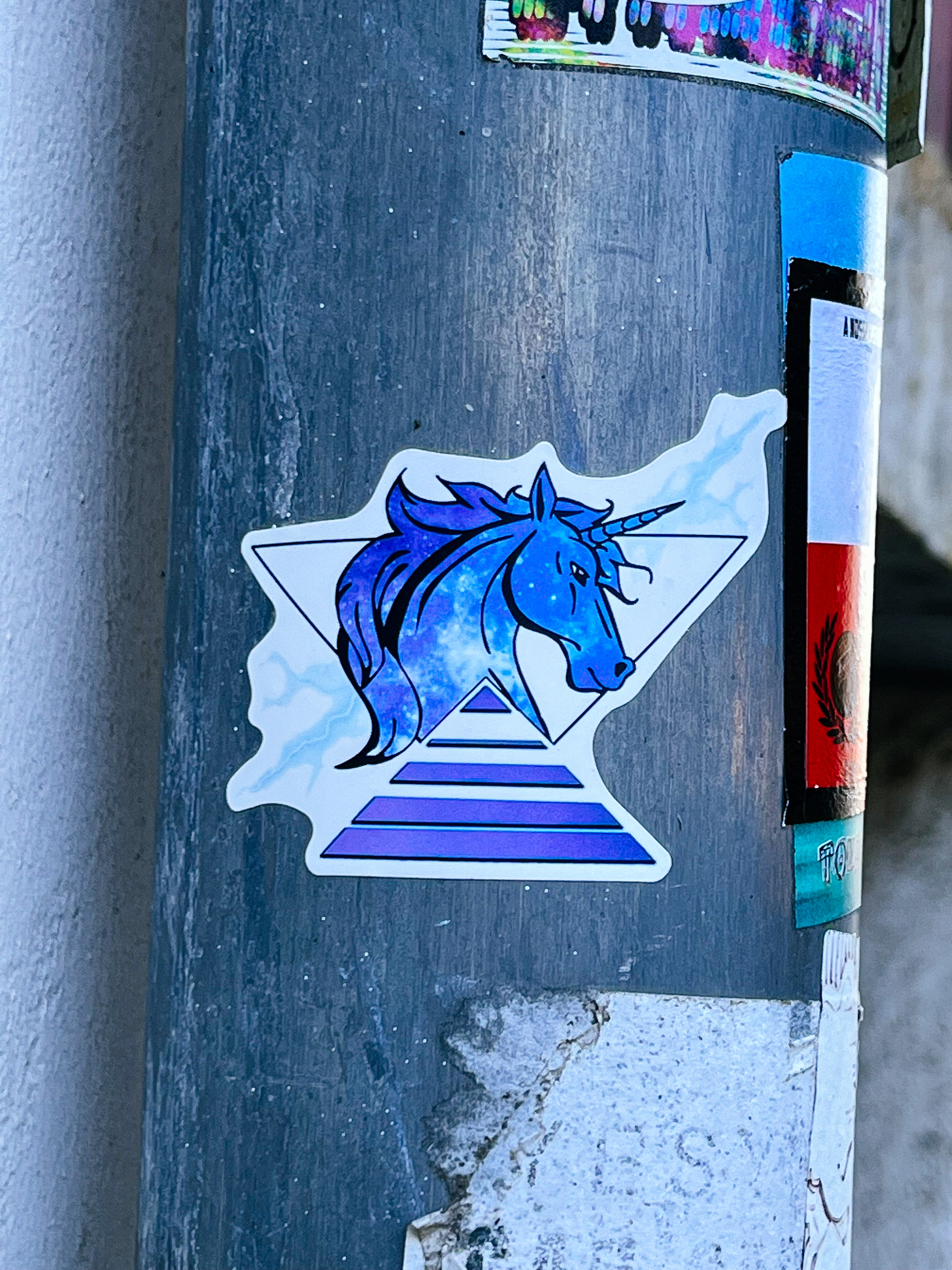 Sticker of a blue unicorn head, with a triangle beneath it. 