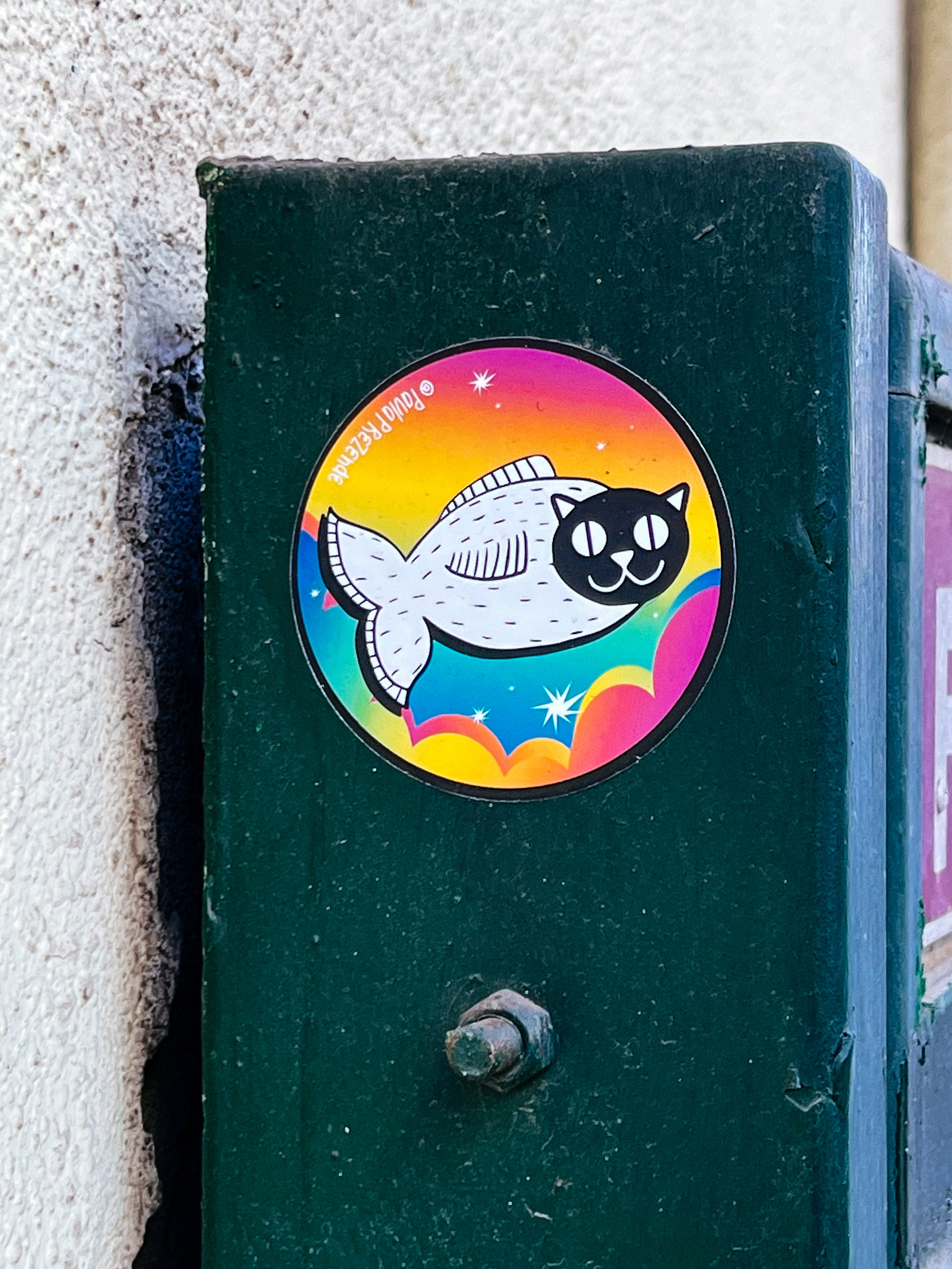 Sticker of a cartoonish fish, with a cat’s head. The background is colorful. 