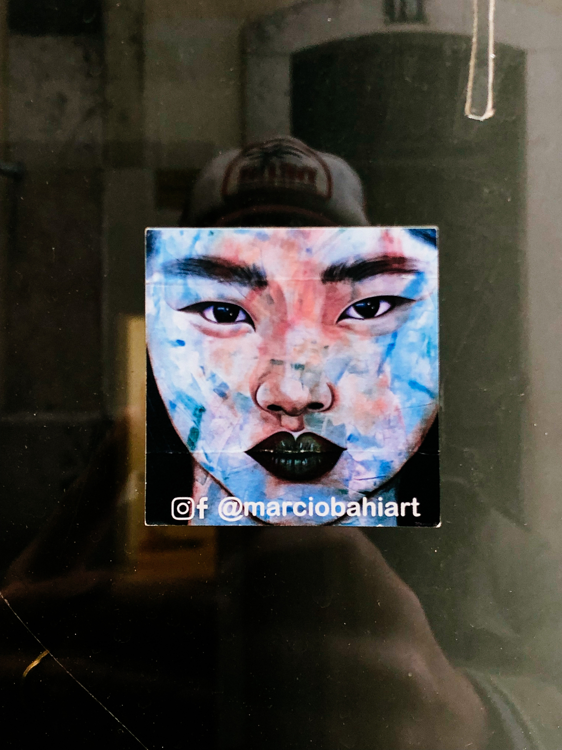 Sticker of a face with lips painted with black lipstick, and some blue streaks over the face. 