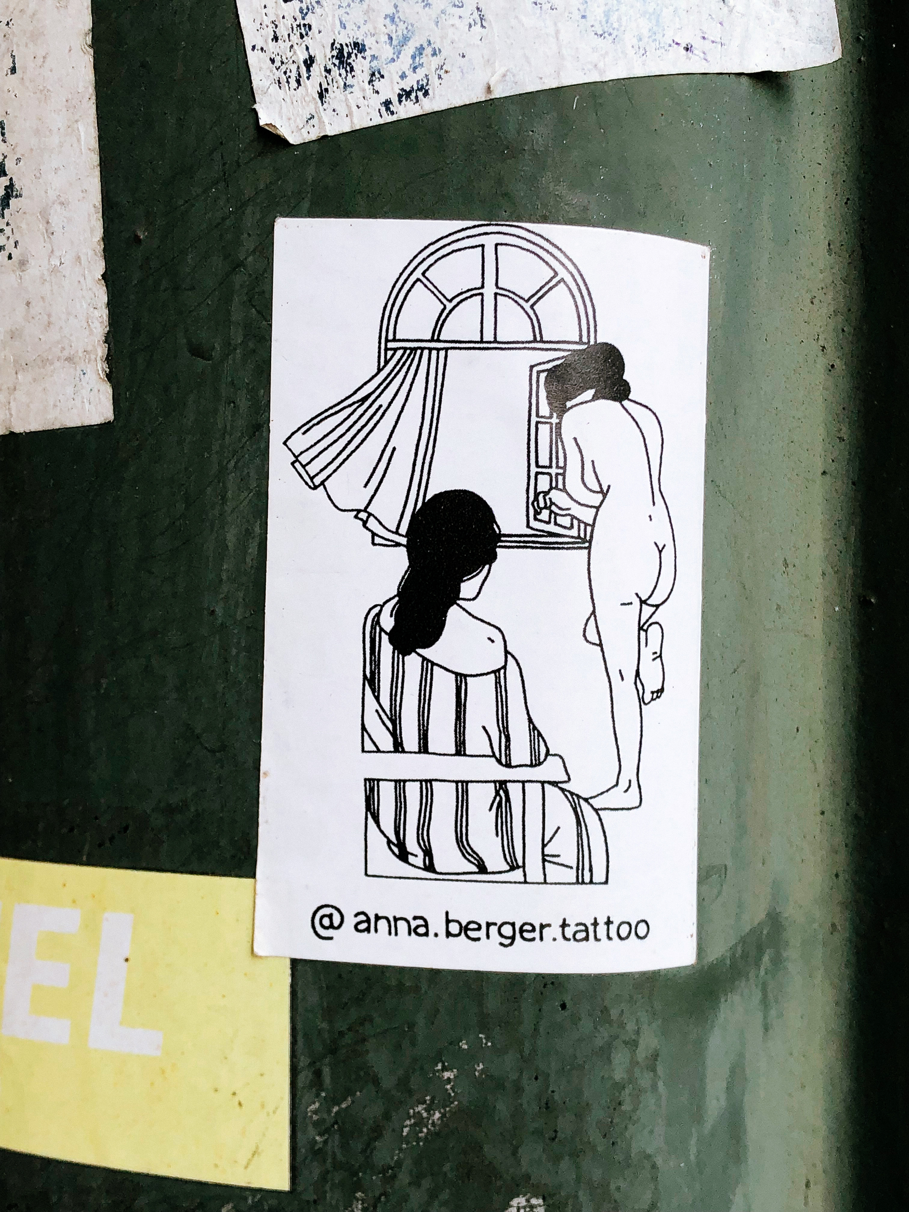 Sticker with a drawing of two women seen from the back. One is sitting down, the other standing up, naked, looking out a window. 