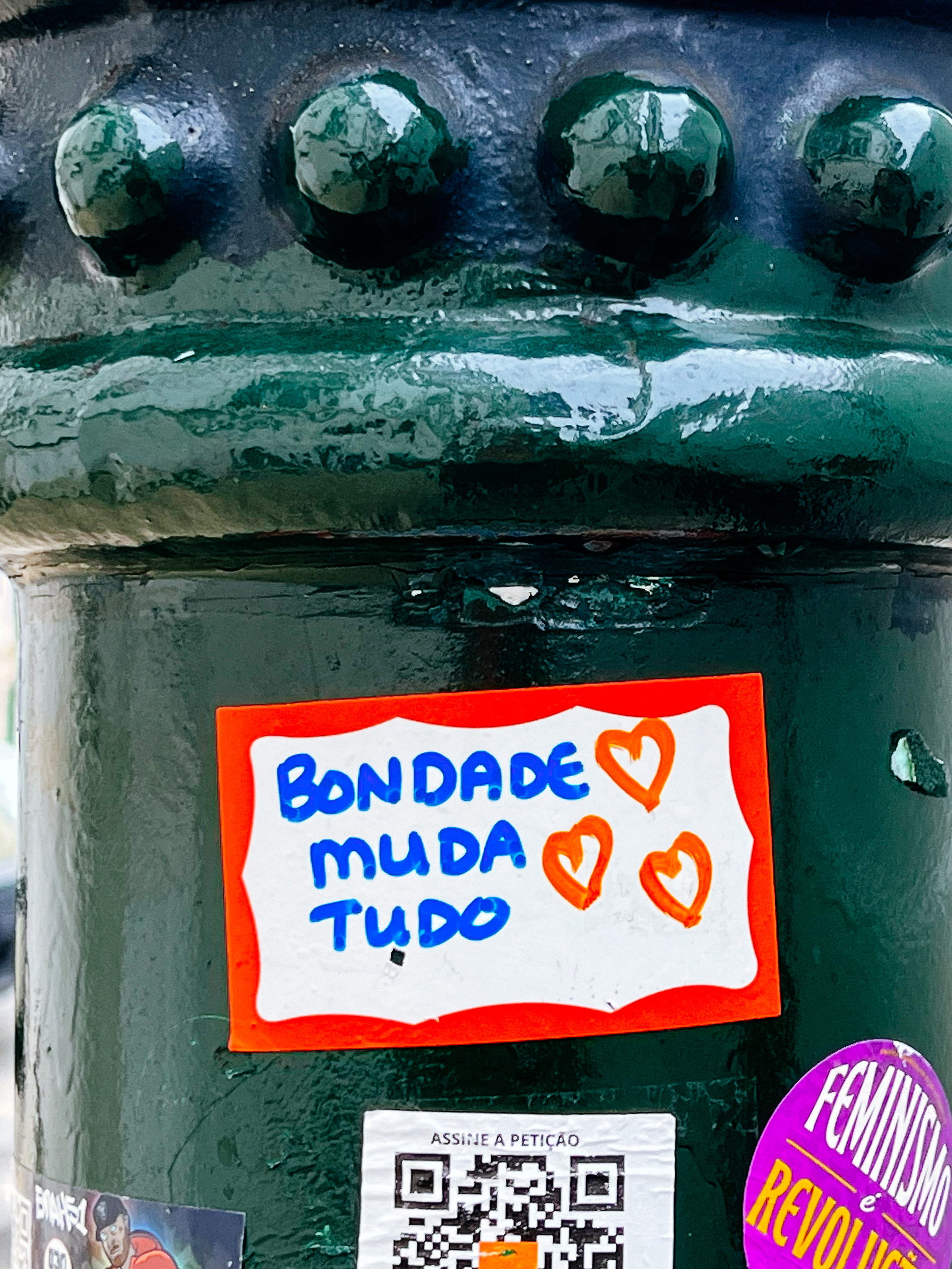 Sticker with three hand drawn hearts, and the words “Bondade muda tudo” (Kindness changes everything).