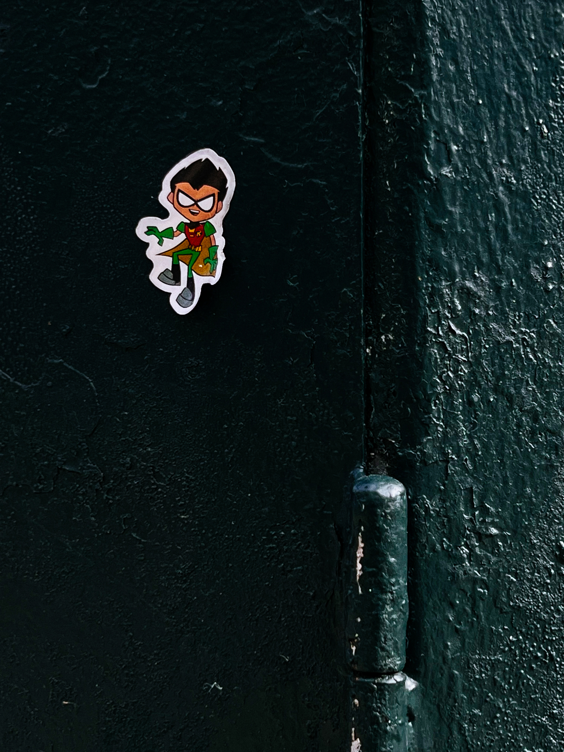 A tiny super hero sticker on a dark green metal box 