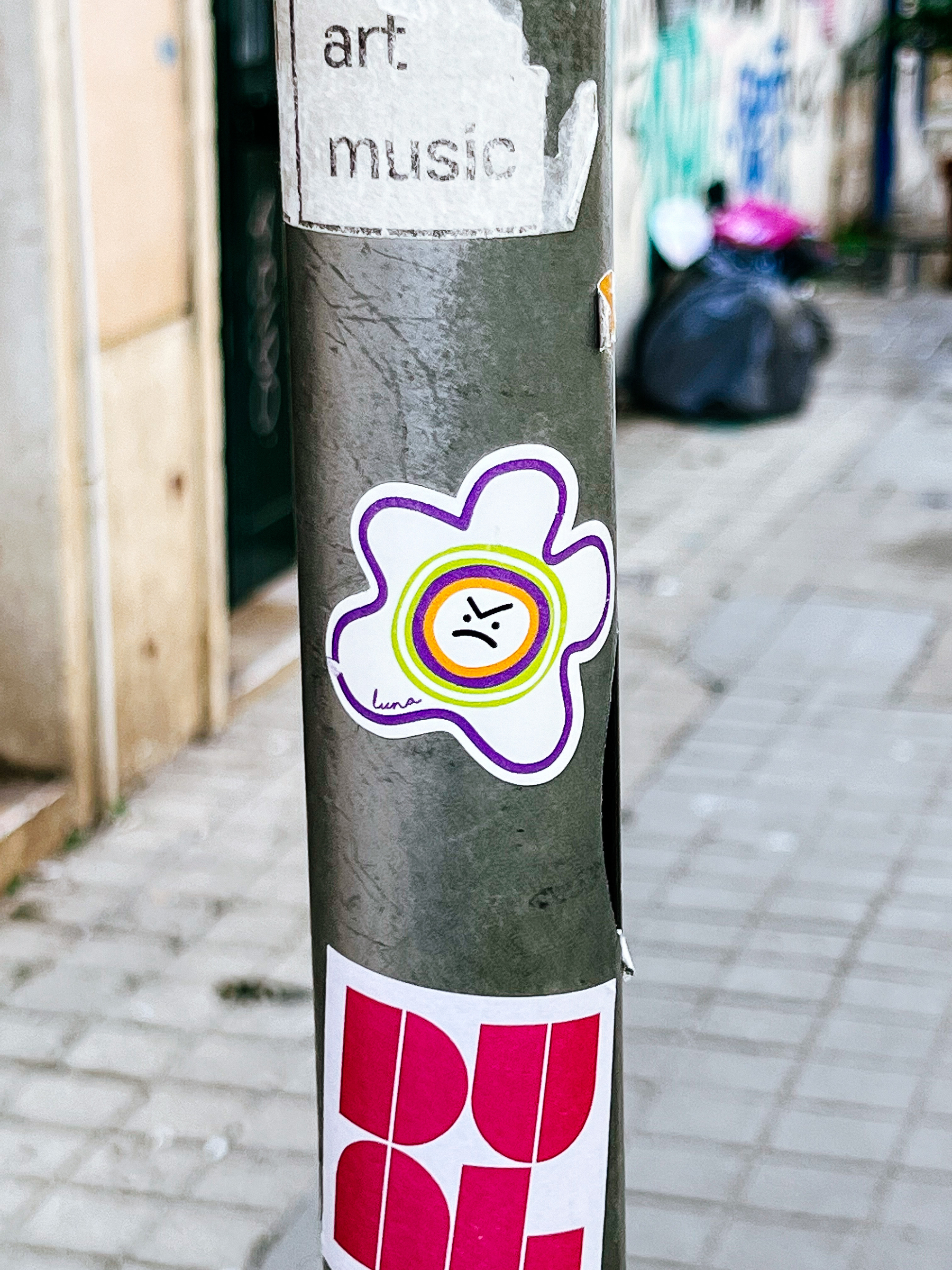 A “flowery”/fried egg design, with a very angry face in the middle. Stuck to a post. 