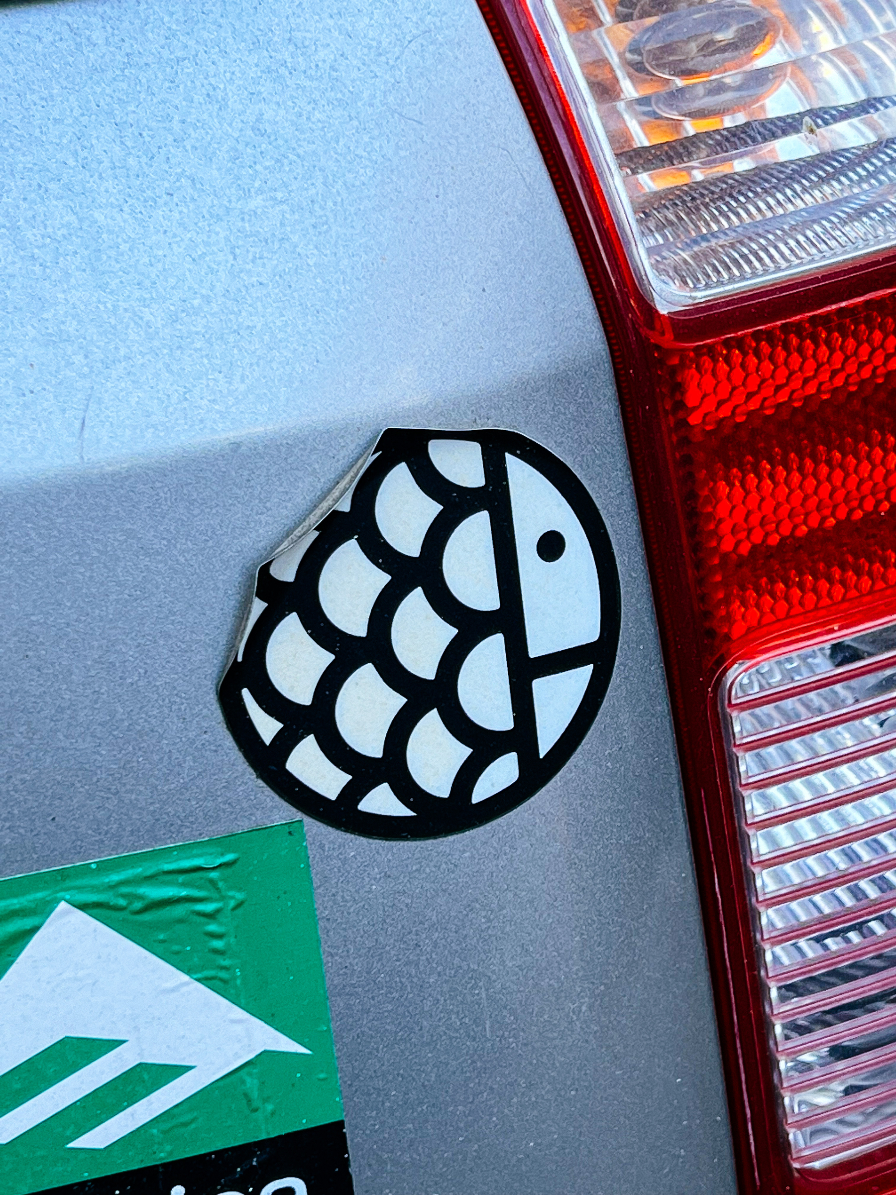 Round sticker on a car, depicting a cute fish. 