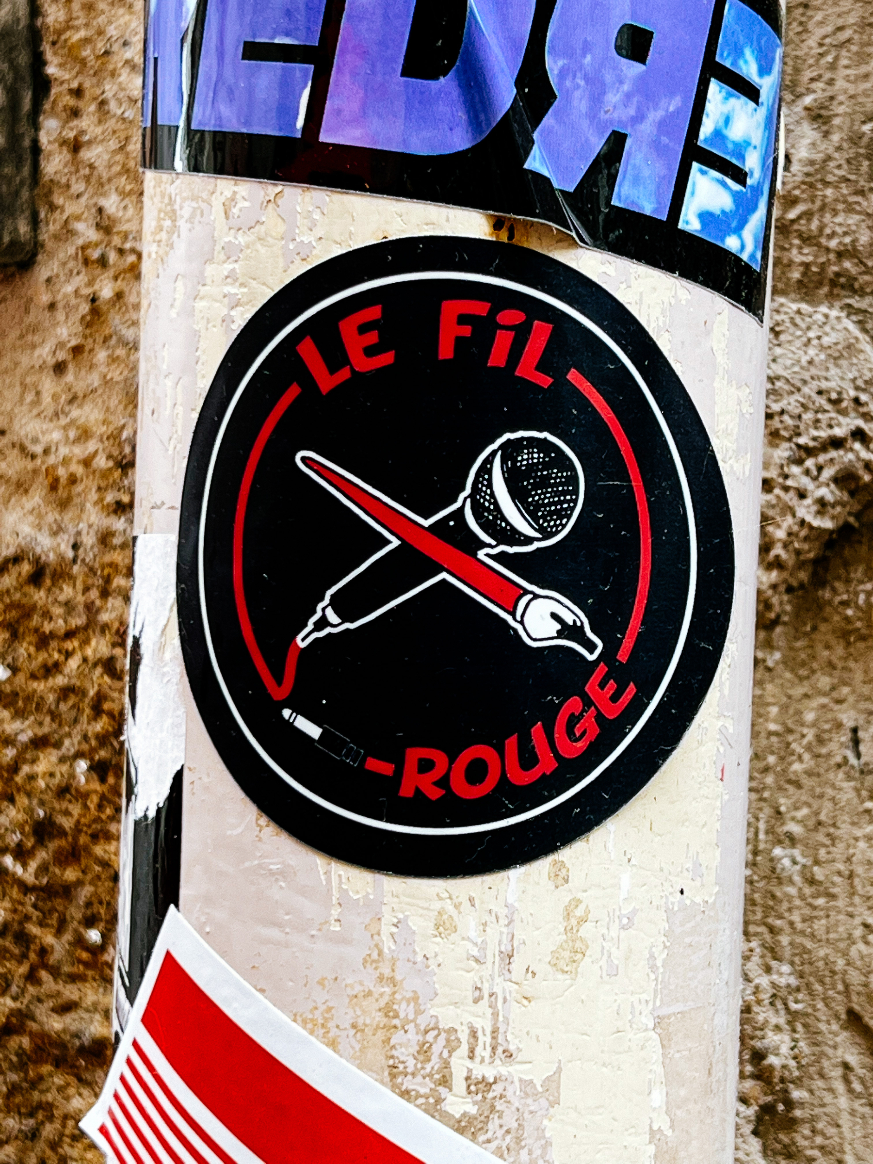 Sticker of a microphone and a fountain pain, with the words “Le fil rouge” written on it. 