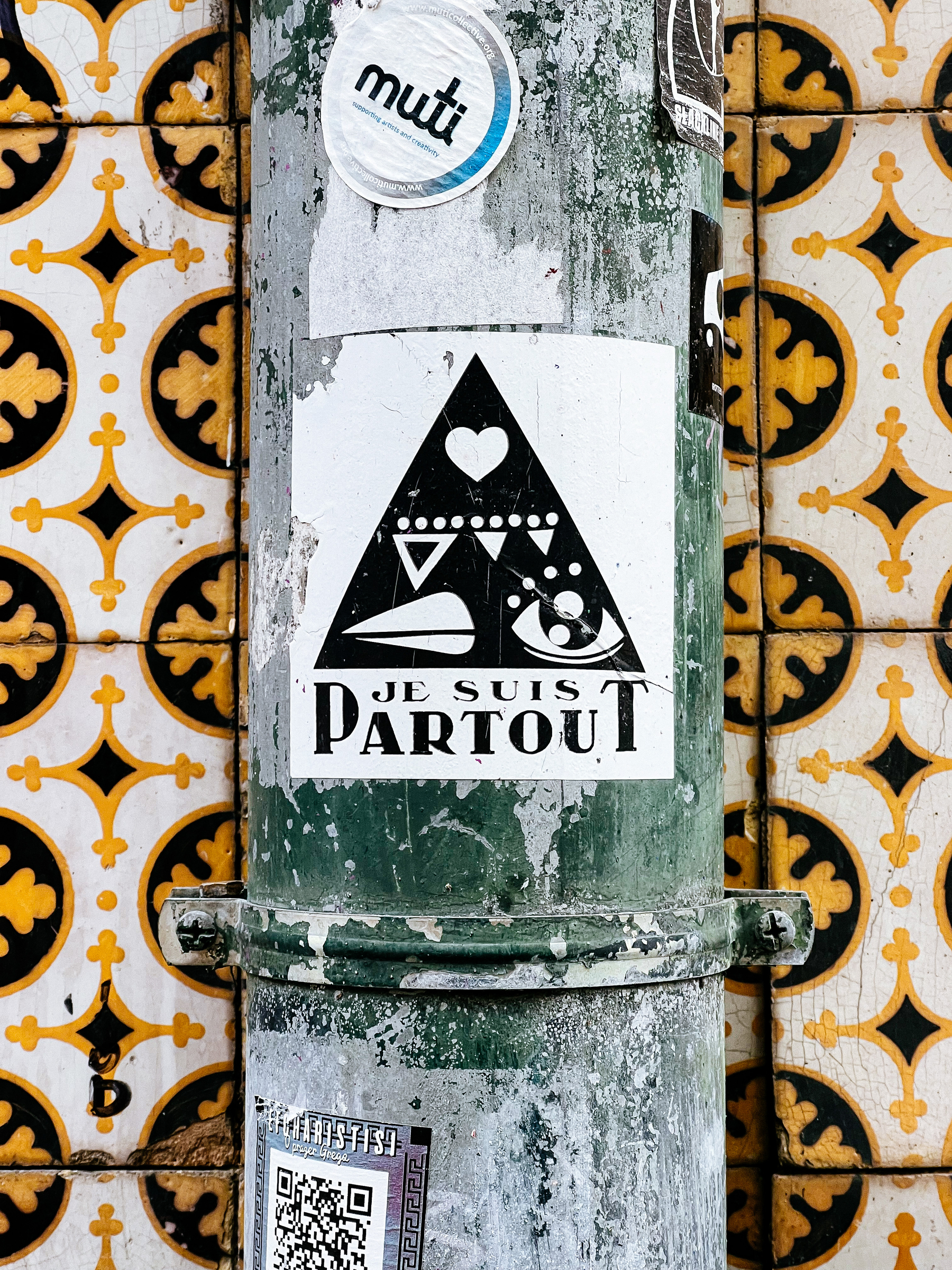 Sticker with the words “je suis partout”, and a black triangle with symbols inside. One of them is a heart 