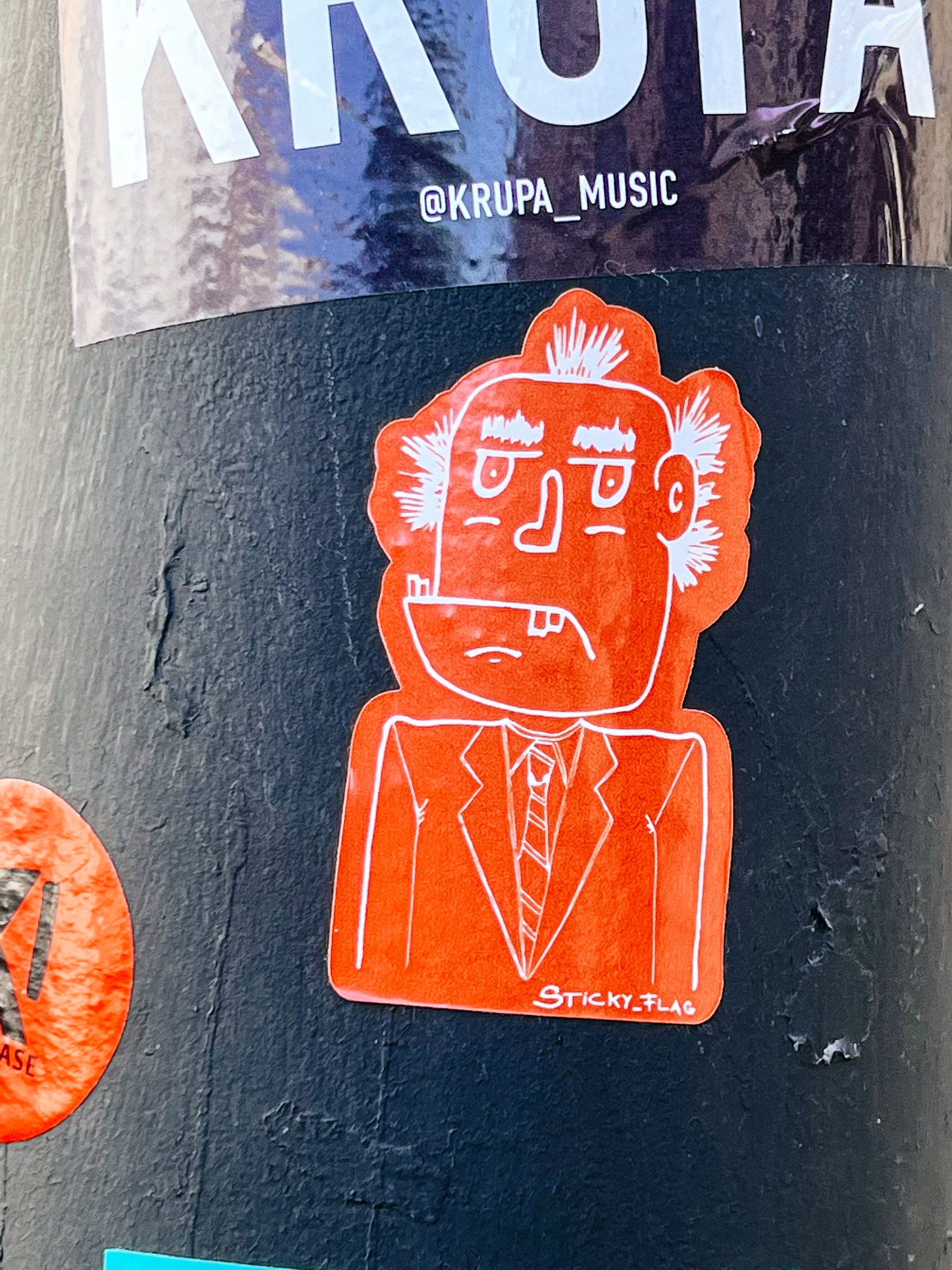 Sticker of a drawing of a grumpy old man, probably some cartoon character I’m not familiar with. Red background, white line. 