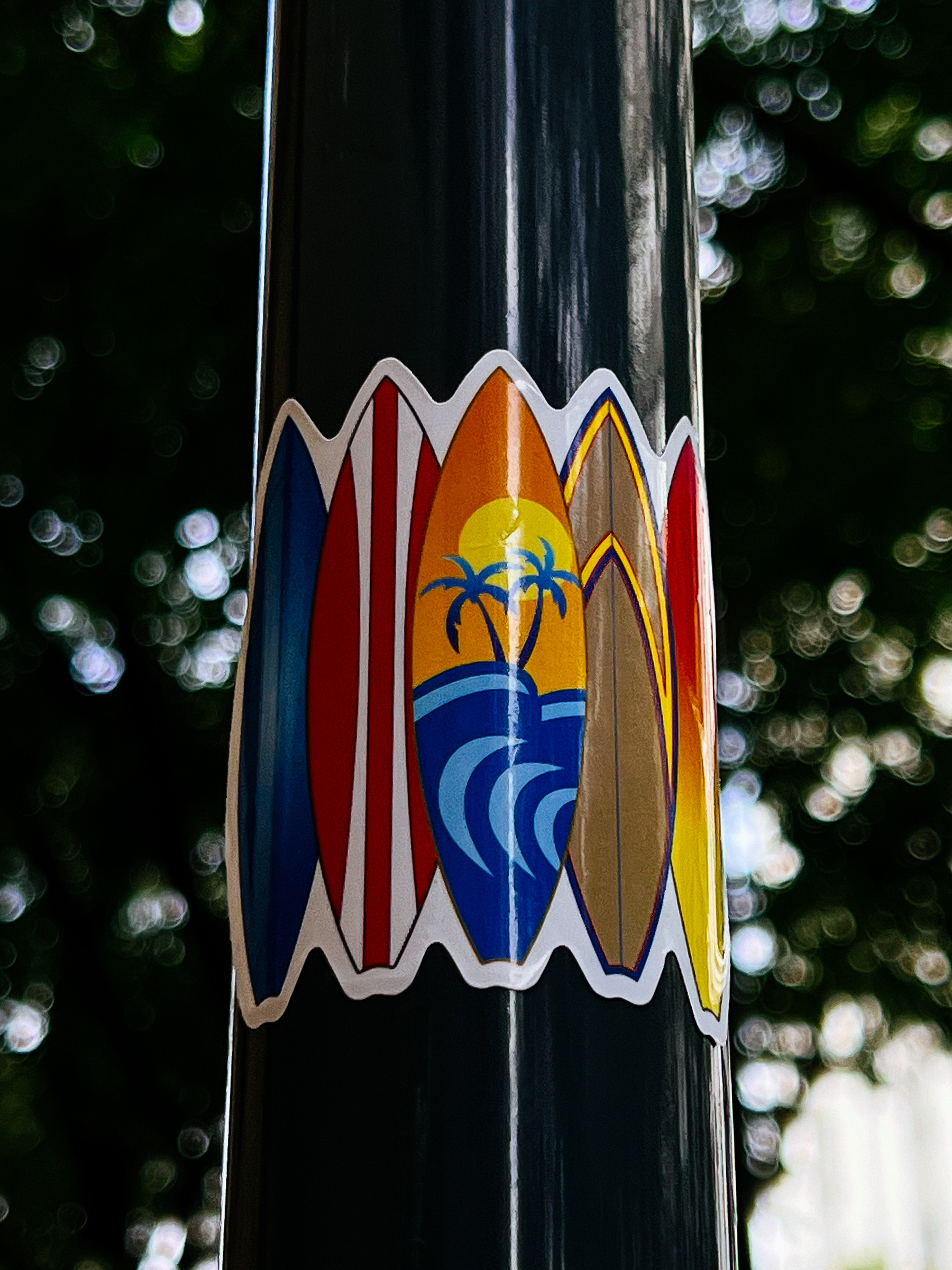 Sticker with five surfboards in a row. The middle one has palm trees, and the sea. 