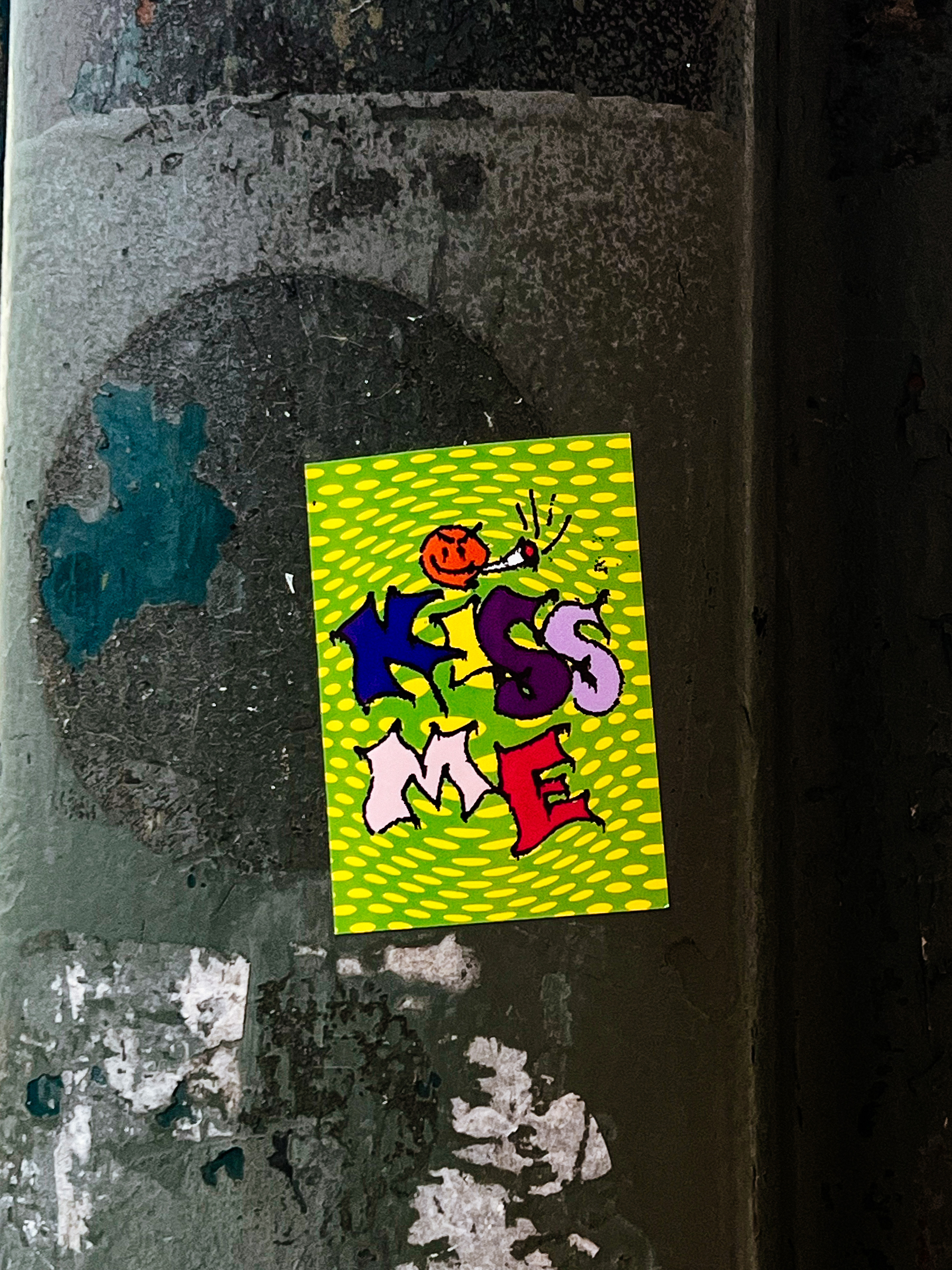 Sticker with “kiss me” written on it, and a tiny smoking smiley above that. 