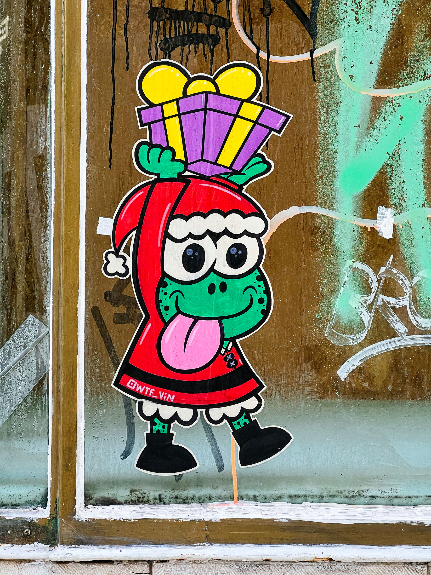 Sticker of a cartoon frog dressed as Santa, carrying a present. 