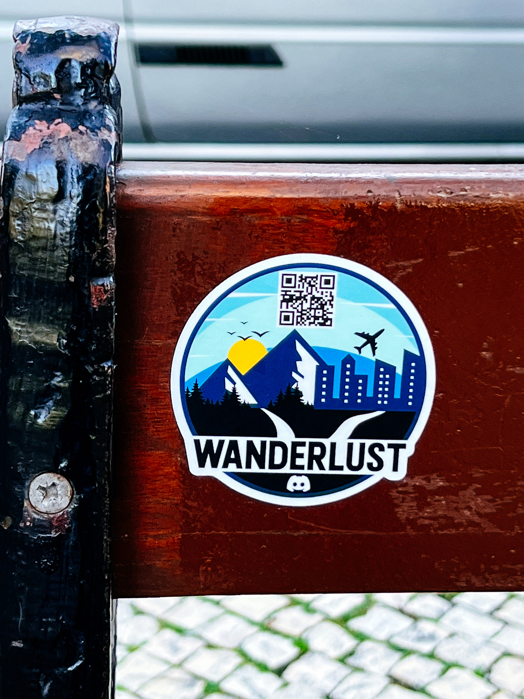 Sticker with the word “wanderlust”, and a landscape, complete with mountains, city skyline, airplane, birds, and even the sun. 