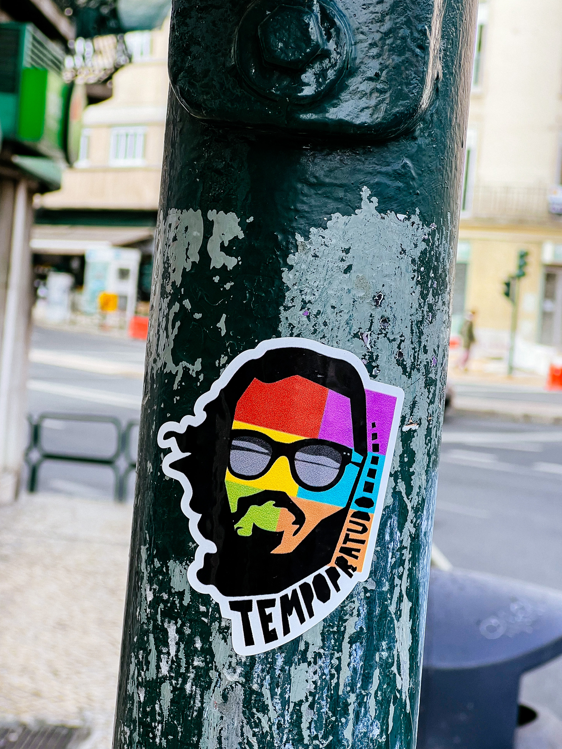 Sticker with the drawing of a man’s face, full of color, and the word “tempoparatudo” (timeforeverything) written on it. 