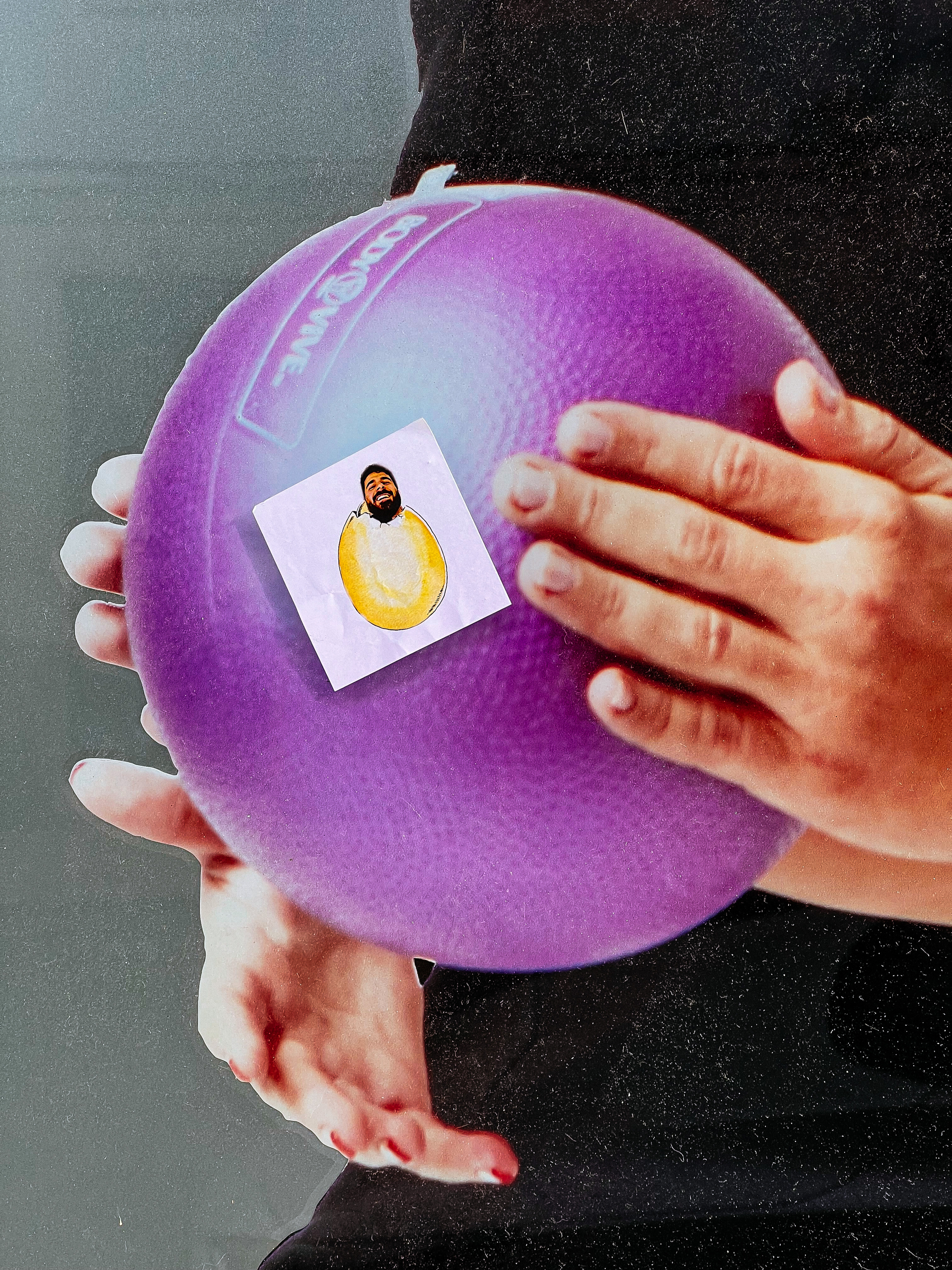 A sticker of a bearded man’s head sticking out of an egg is glued onto a photo of hands holding a purple ball. Odd, but true. 
