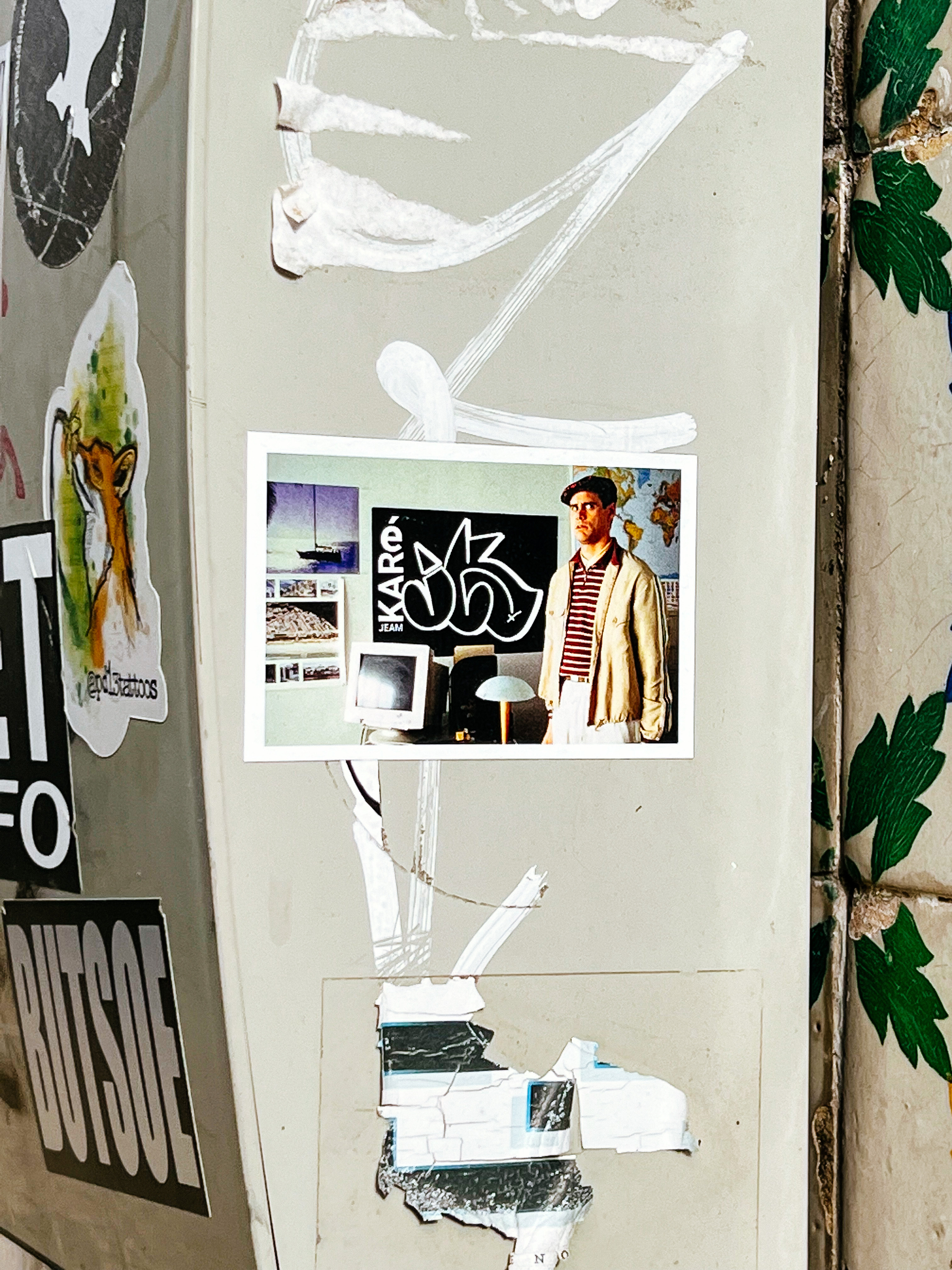 Sticker with the photo of a man looking at us, standing in a room with a computer and a desk. 