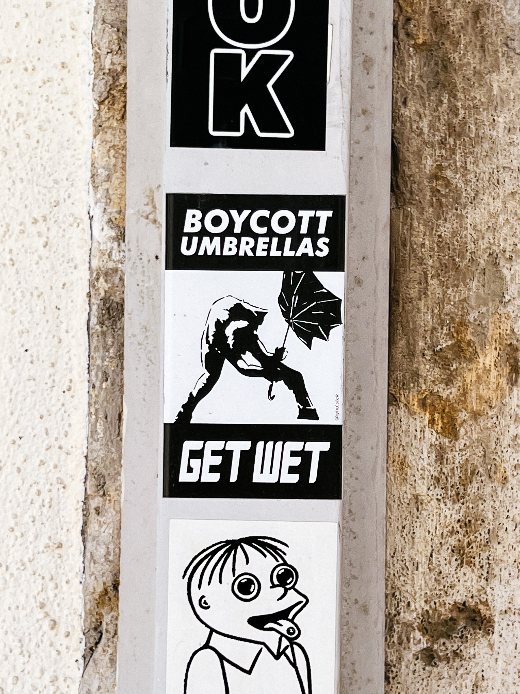 Drawing of a man struggling with an umbrella in the wind. The words “boycott umbrellas, get wet”. 